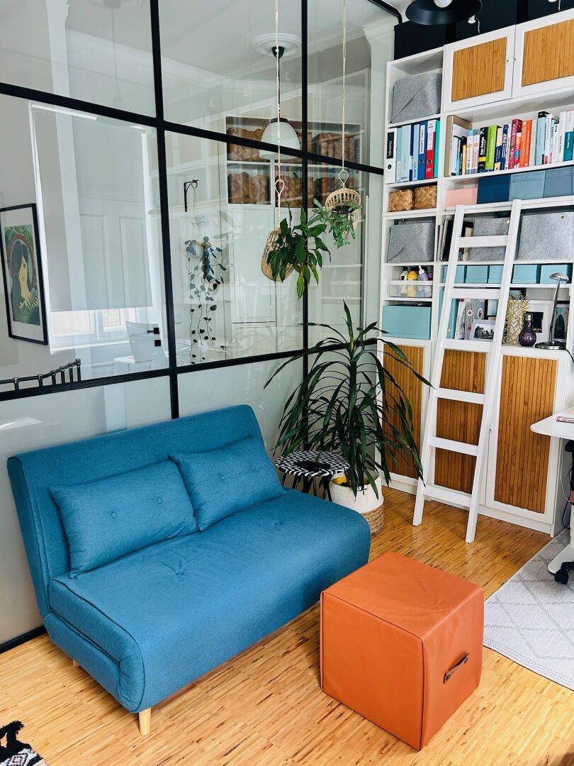 Heller Arbeitsbereich mit blauer Couch, Bücherregal und Glaswand, die den Raum abtrennt.