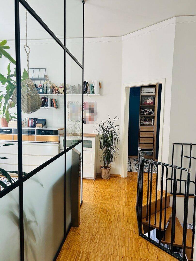 Heller Flur mit Glaswand, die den Arbeitsbereich abtrennt, und einer Wendeltreppe.