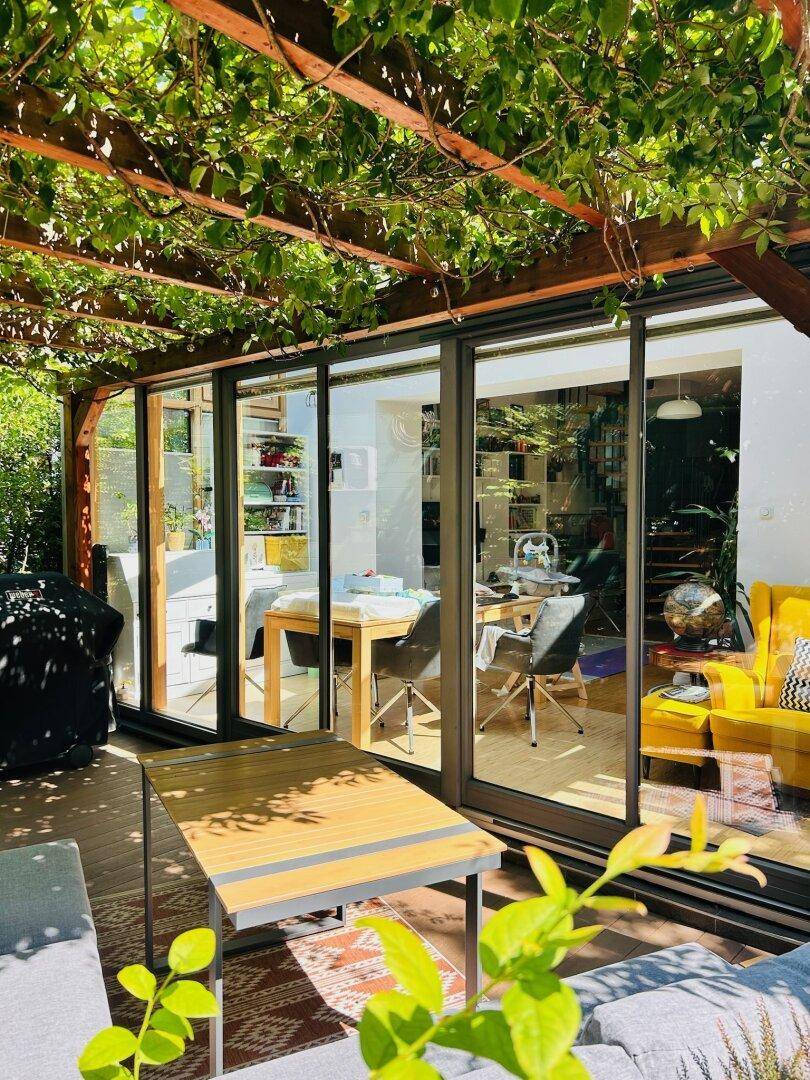 Sonniger Terrassenbereich mit Loungemöbeln und Blick durch die Glasfront in den Wintergarten.
