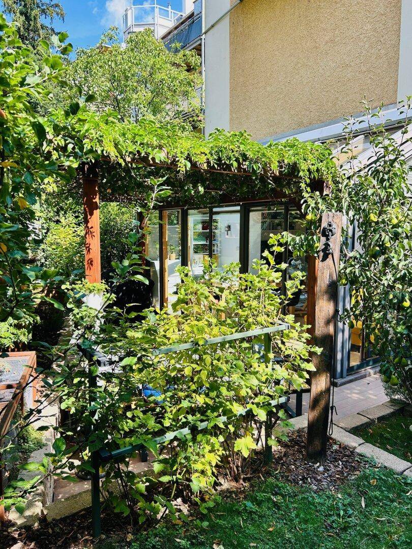 Außenansicht des Hauses mit üppigem Grün, Bäumen und einer überdachten Terrasse.