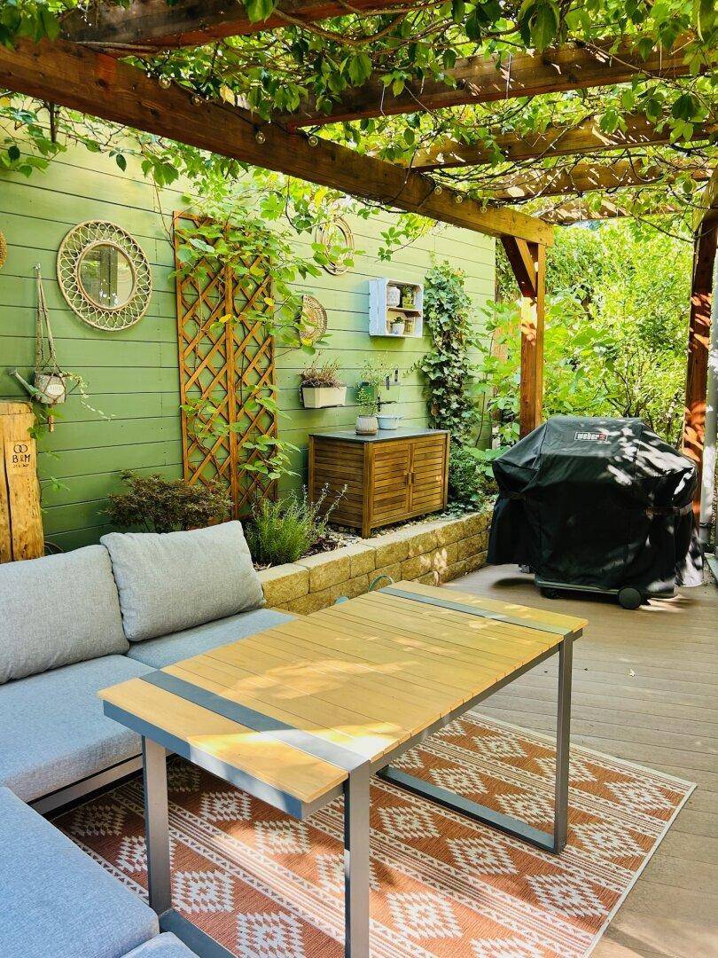 Gemütliche Terrasse mit Pergola, Sitzbereich und Grill, umgeben von üppigem Grün.