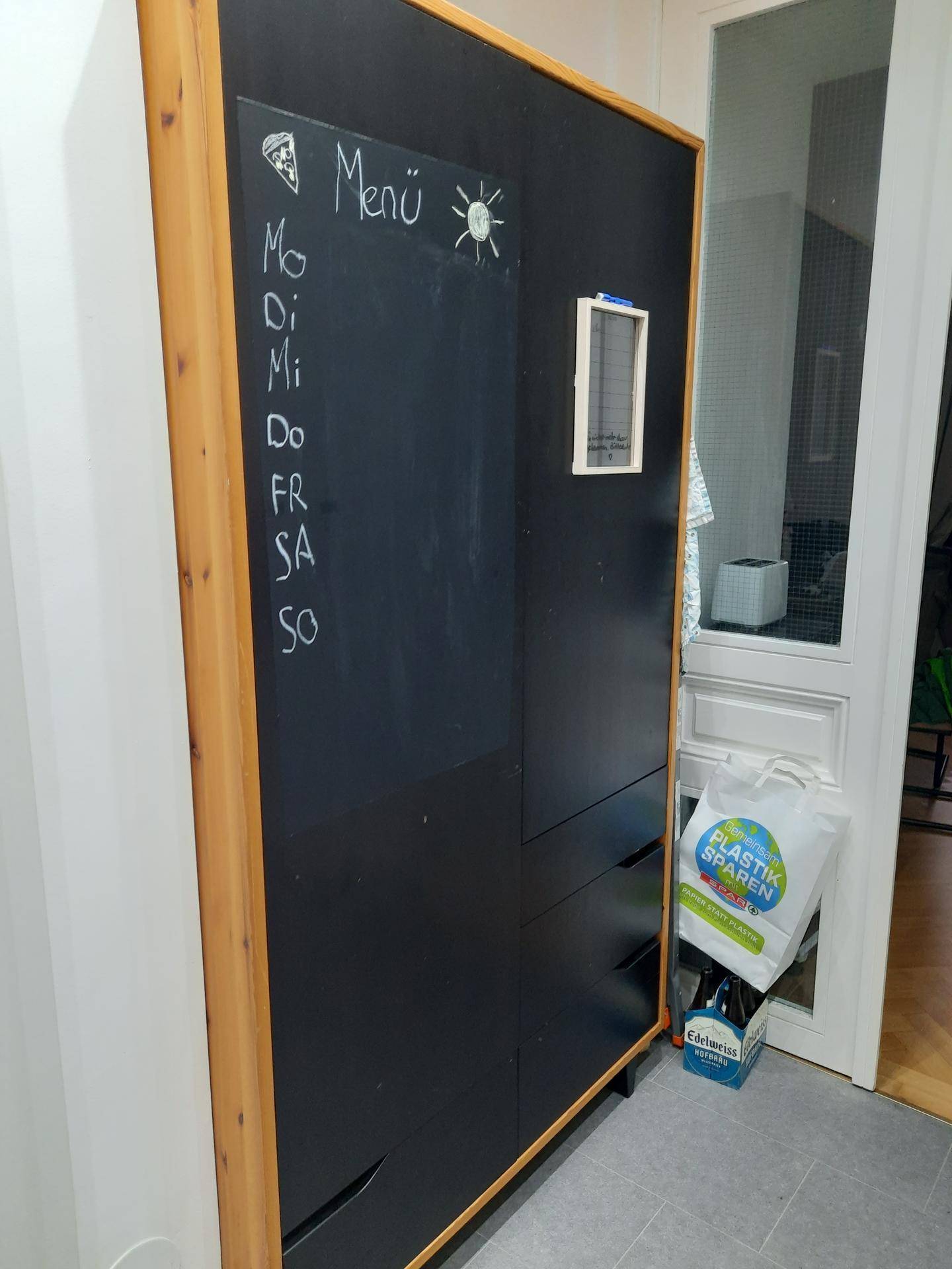 Schwarzer Kreidetafel-Schrank mit Holzrahmen und einer Menüliste, neben einer Tür.