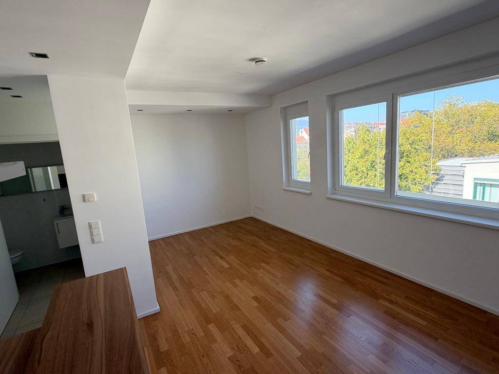 Lichtdurchflutetes Zimmer mit Parkettboden, weißen Wänden und Blick ins Grüne.