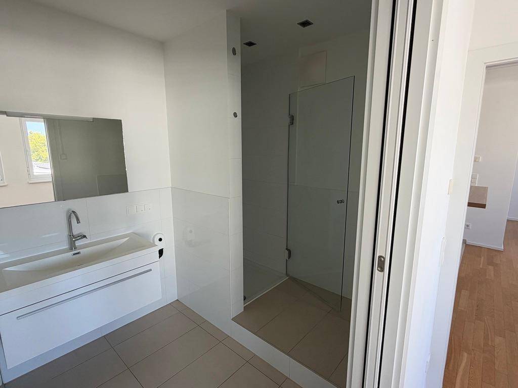 Helles Badezimmer mit ebenerdiger Dusche, großem Waschbecken und Fliesenboden.