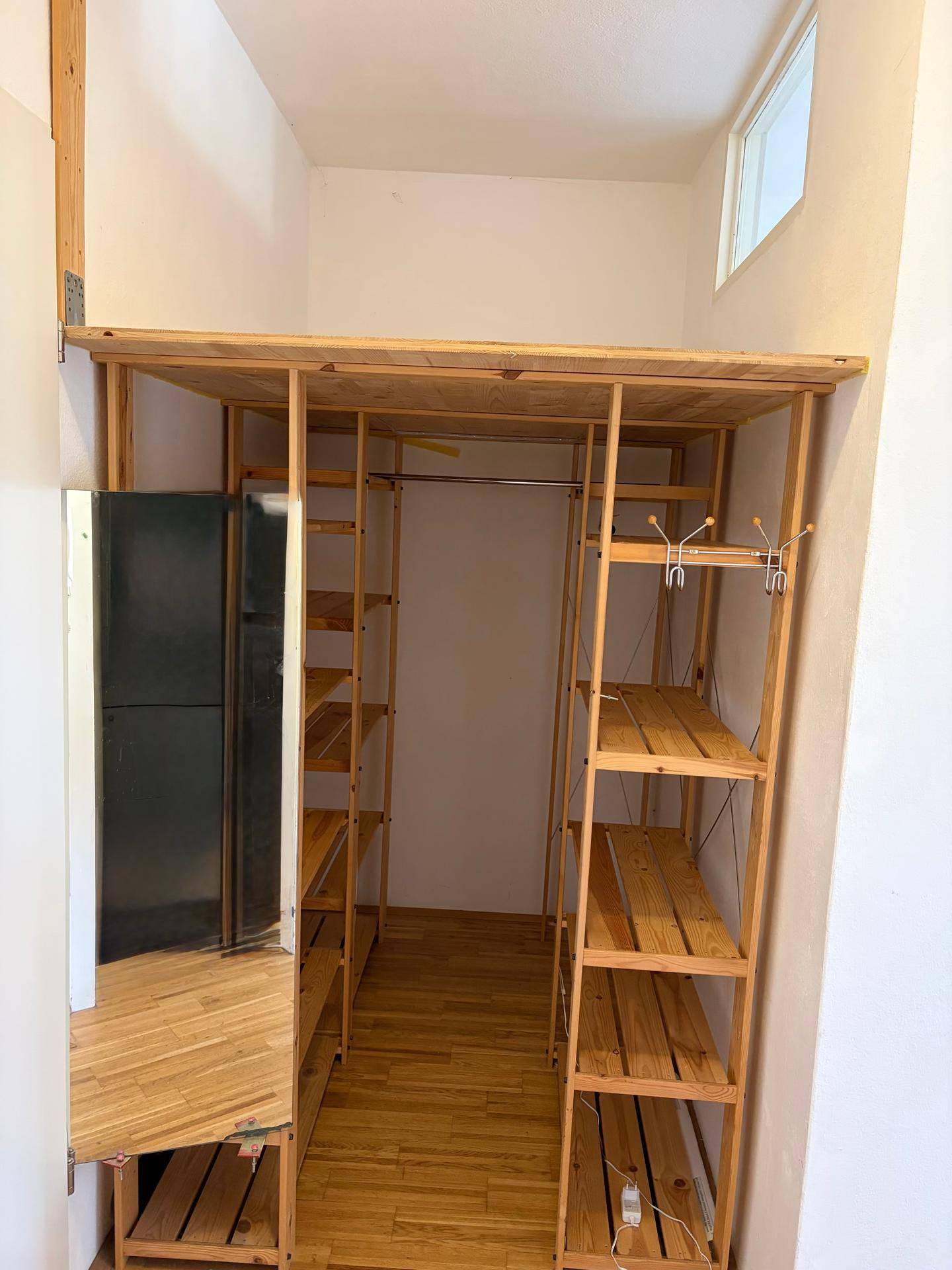 Praktischer Abstellraum mit offenen Holzregalen und einem Kühlschrank für zusätzlichen Stauraum.
