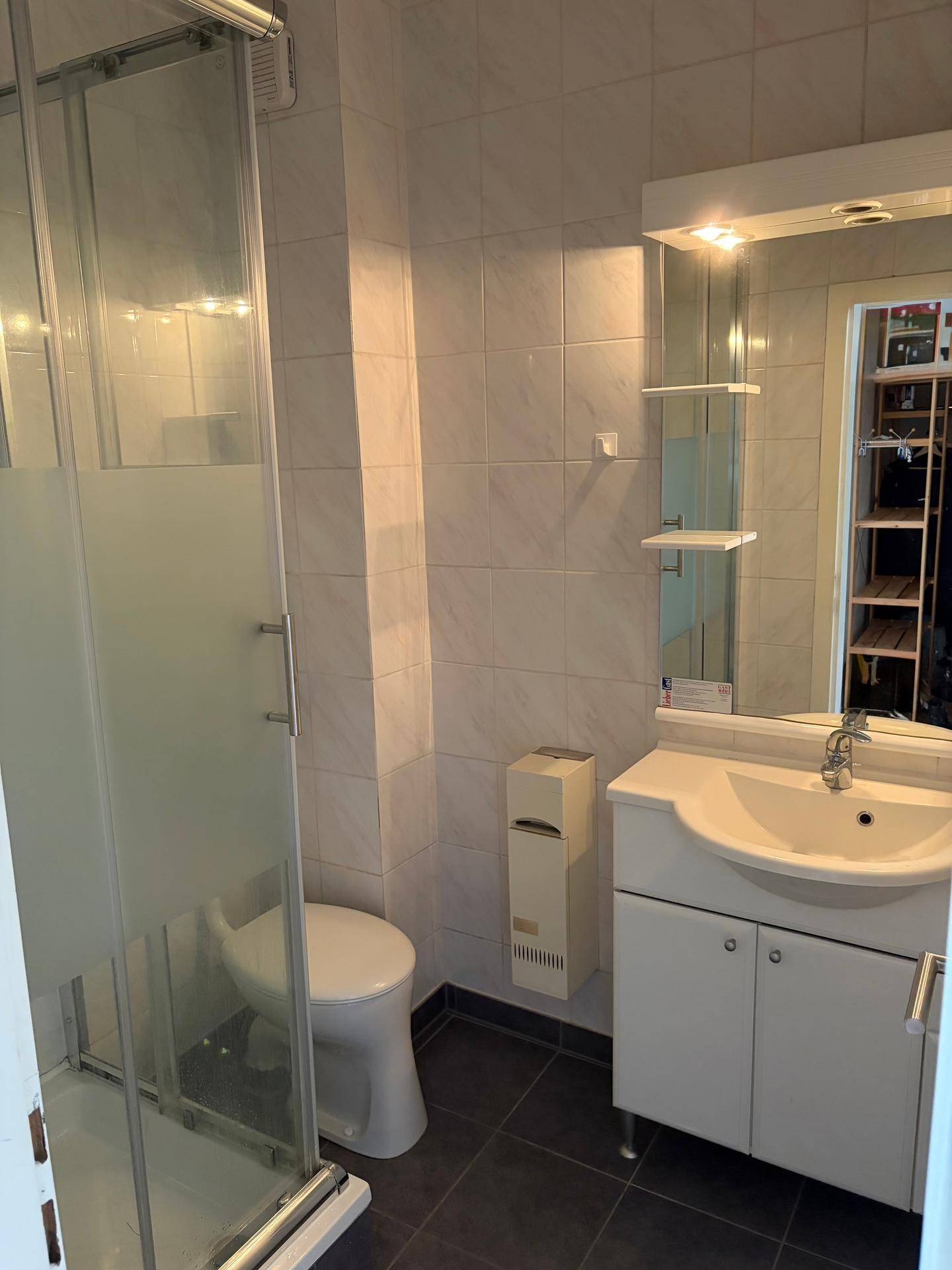 Modernes Badezimmer mit Duschkabine, Waschbecken und hellen Fliesen an Wänden und Boden.