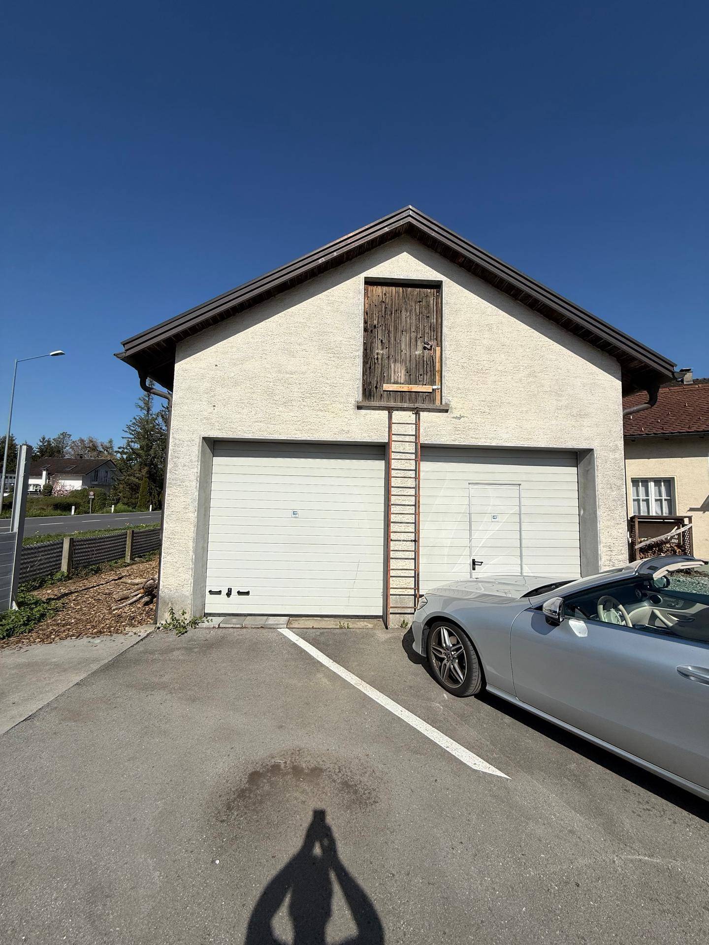 Frontale Außenansicht des Gebäudes mit zwei Garagentoren, einer Leiter und einem geparkten Auto.