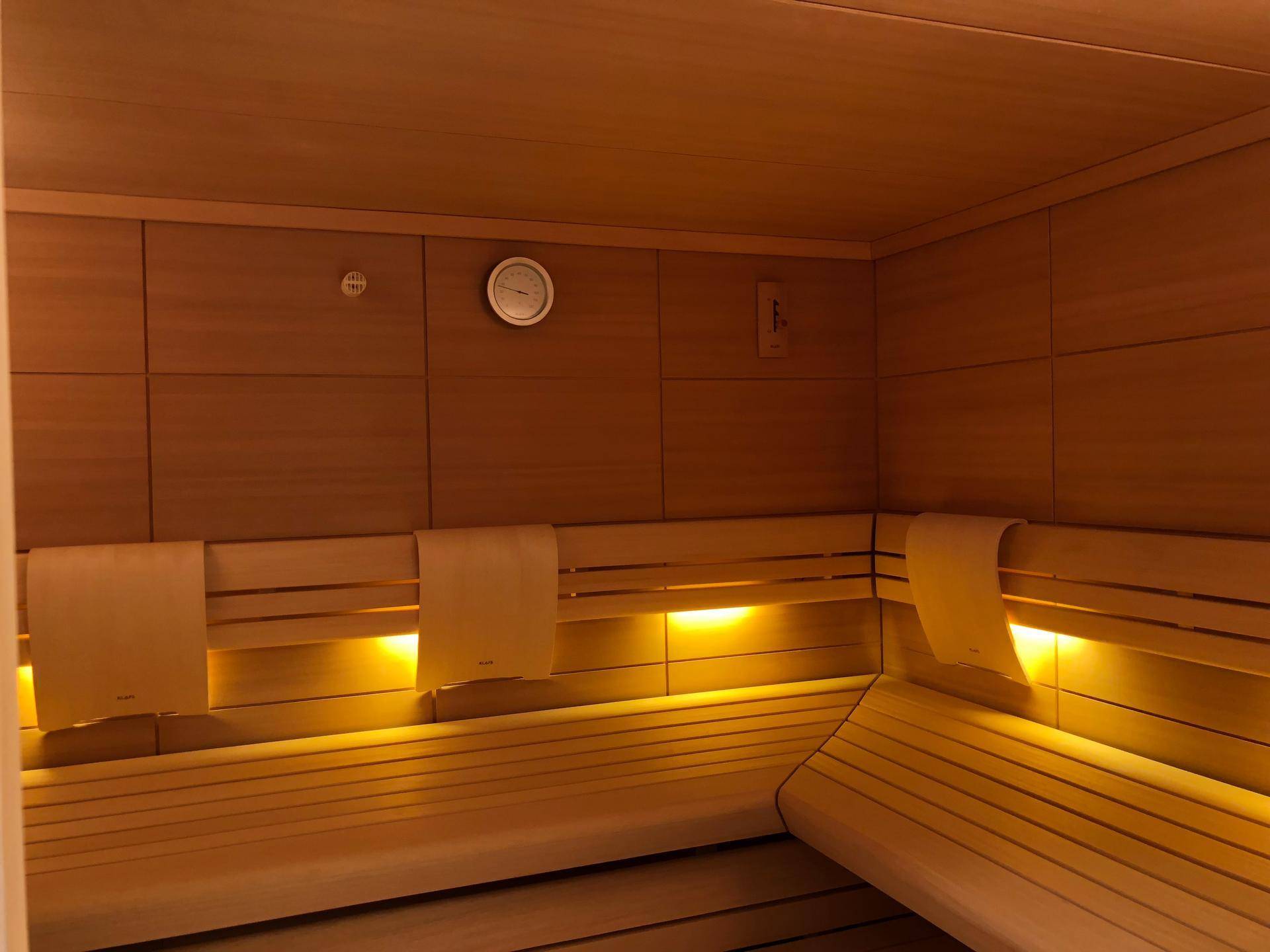 Moderne Holzsauna mit bequemen Bänken, indirekter Beleuchtung und Temperaturanzeige.