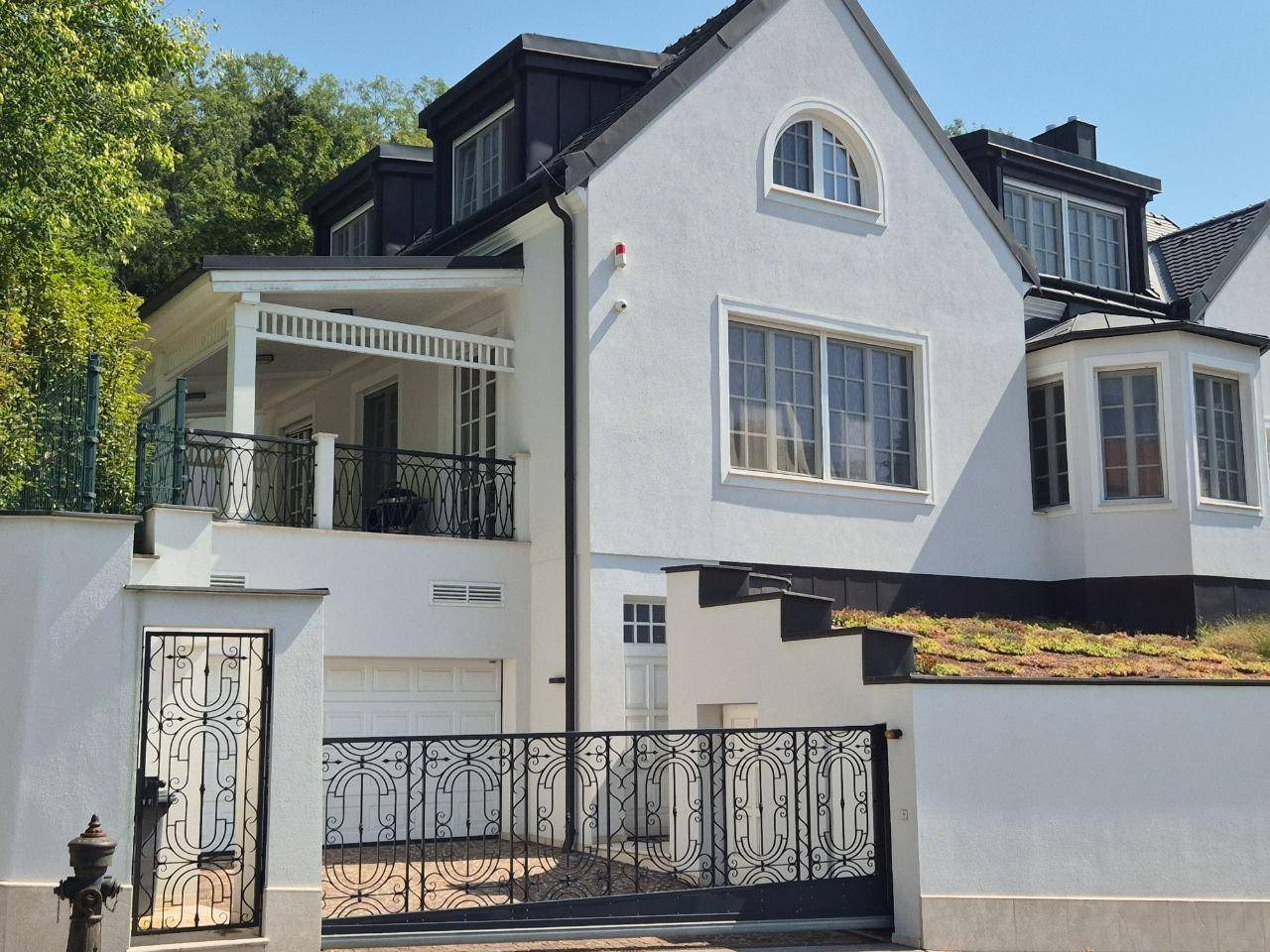 Detailansicht der weißen Villa mit Balkon, schmiedeeisernem Tor und Garagenzufahrt.