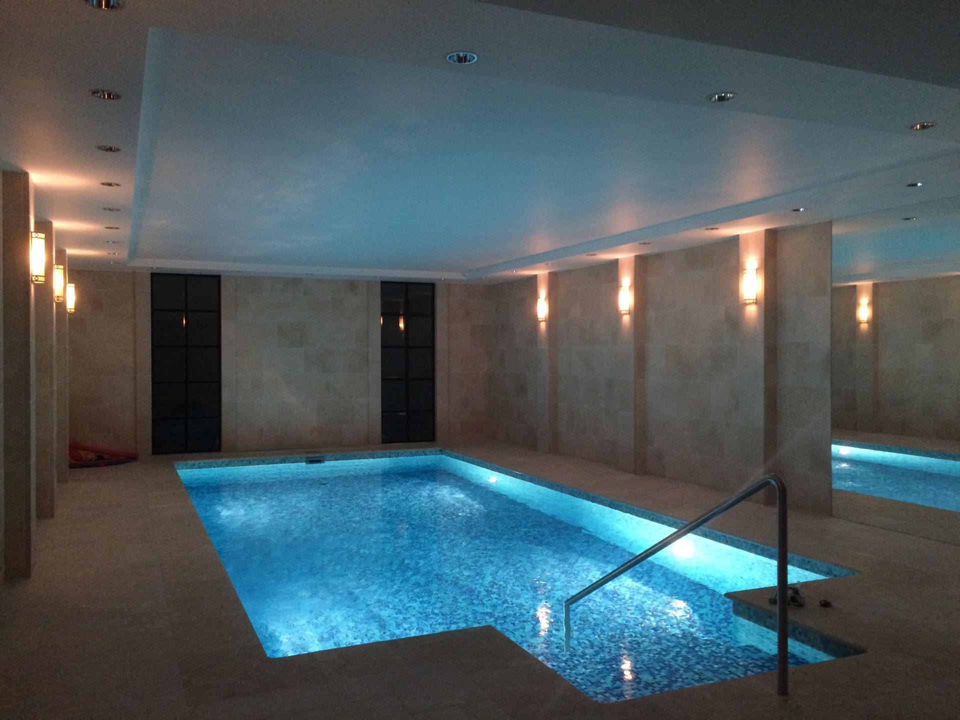 Innenpool mit blauen Mosaikfliesen, indirekter Beleuchtung und beigen Steinwänden.