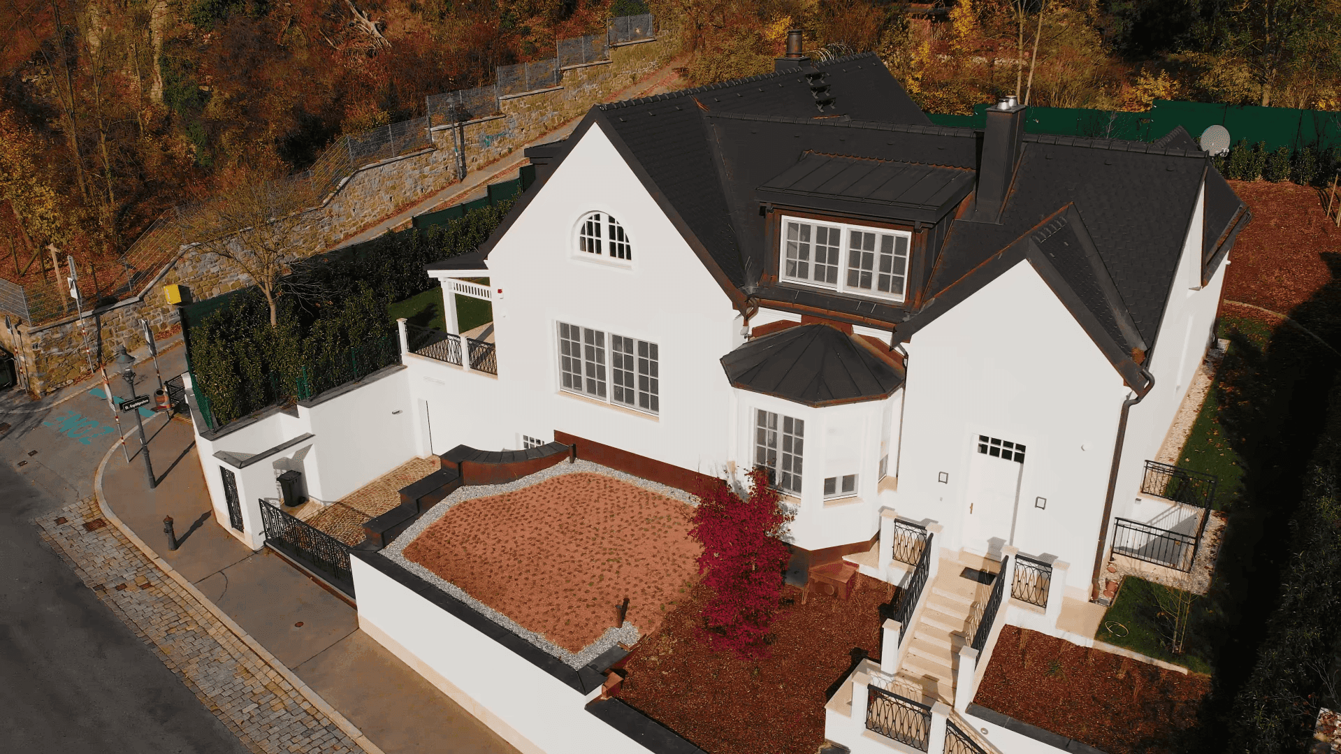 Vogelperspektive der modernen Villa mit schwarzem Dach, weißer Fassade und herbstlicher Gartengestaltung.
