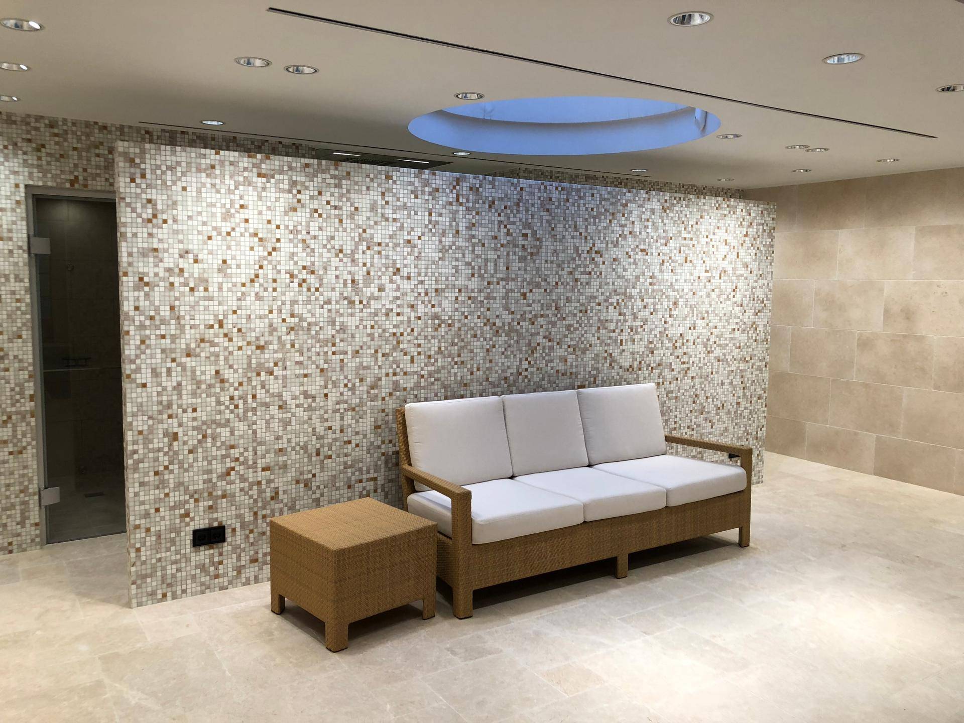 Entspannungsbereich mit Mosaikfliesenwand, beigem Sofa und indirekter Beleuchtung.