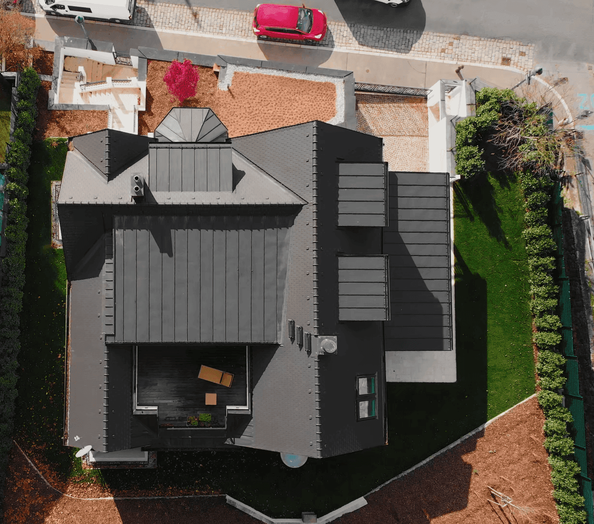 Dachansicht der Villa mit dunklem Ziegeldach, Dachterrassenbereich und umliegendem Garten.