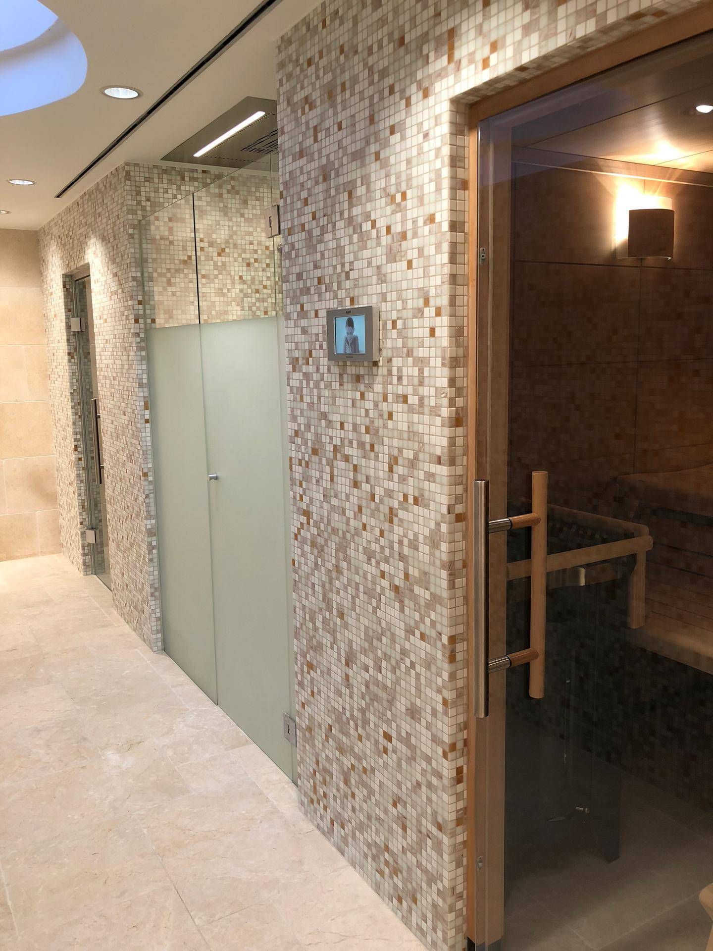 Eingangsbereich zum Wellnessbereich mit Mosaikfliesen, Glaswänden und Zugang zur Sauna.