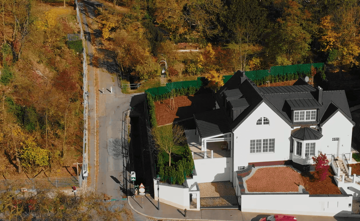 Luftaufnahme der Villa mit umliegender Natur, Straße und angrenzendem Waldgebiet im Herbst.