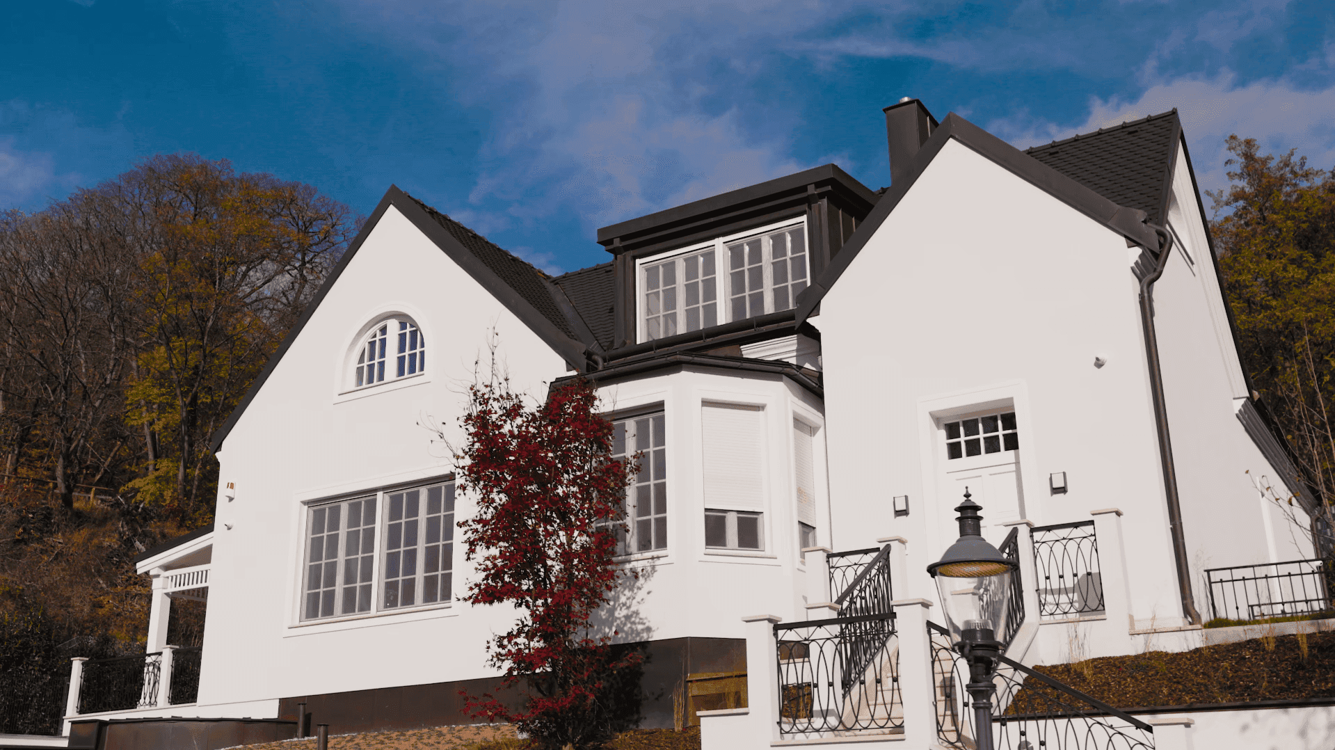 Ansicht der eleganten Villa mit weißer Fassade, großen Fenstern und herbstlicher Bepflanzung.