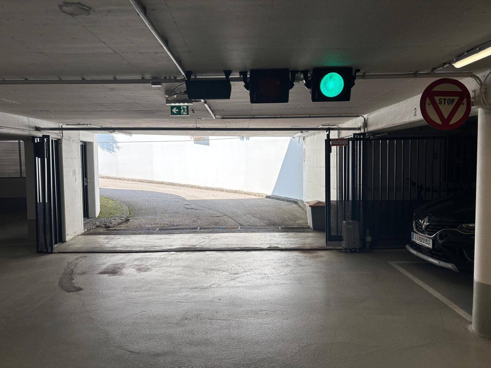 Ausfahrt einer Tiefgarage mit grüner Ampel, Stoppschild und Blick auf die Zufahrtsrampe.