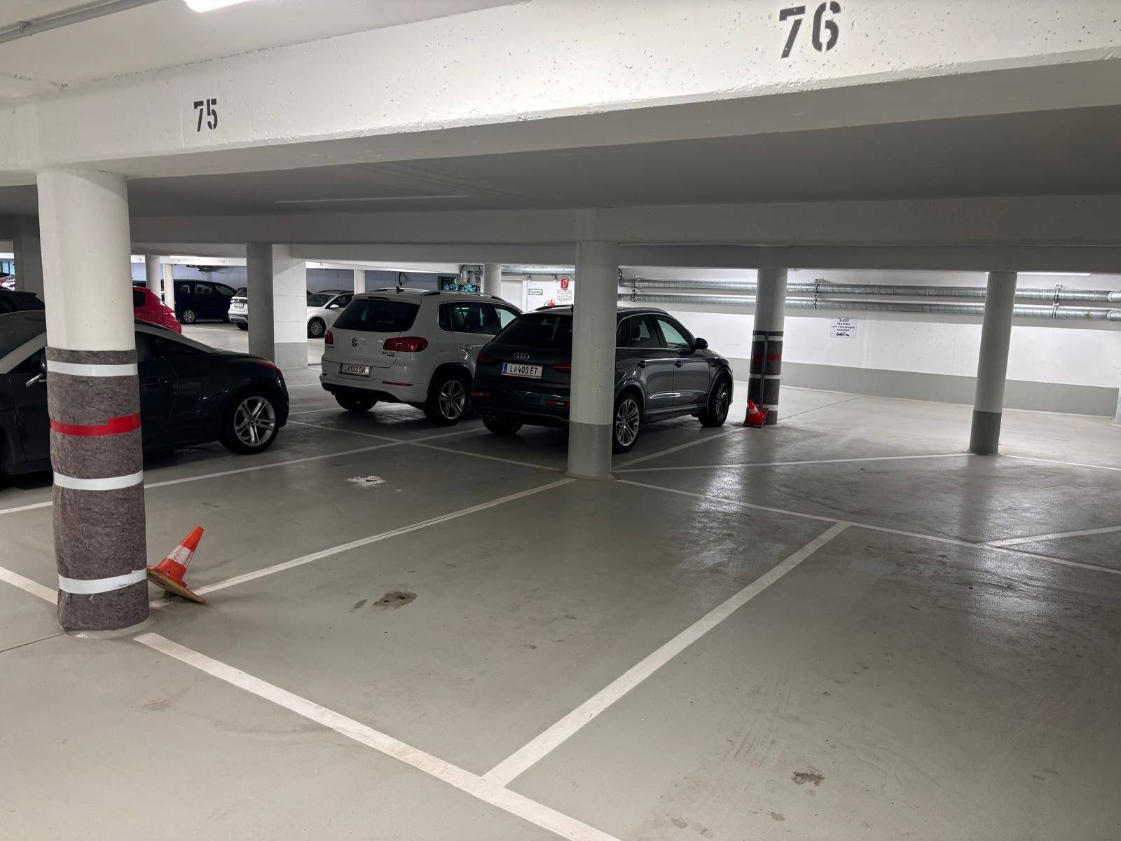 Übersichtliche Tiefgarage mit markierten Parkplätzen, Säulen und einigen geparkten Autos.