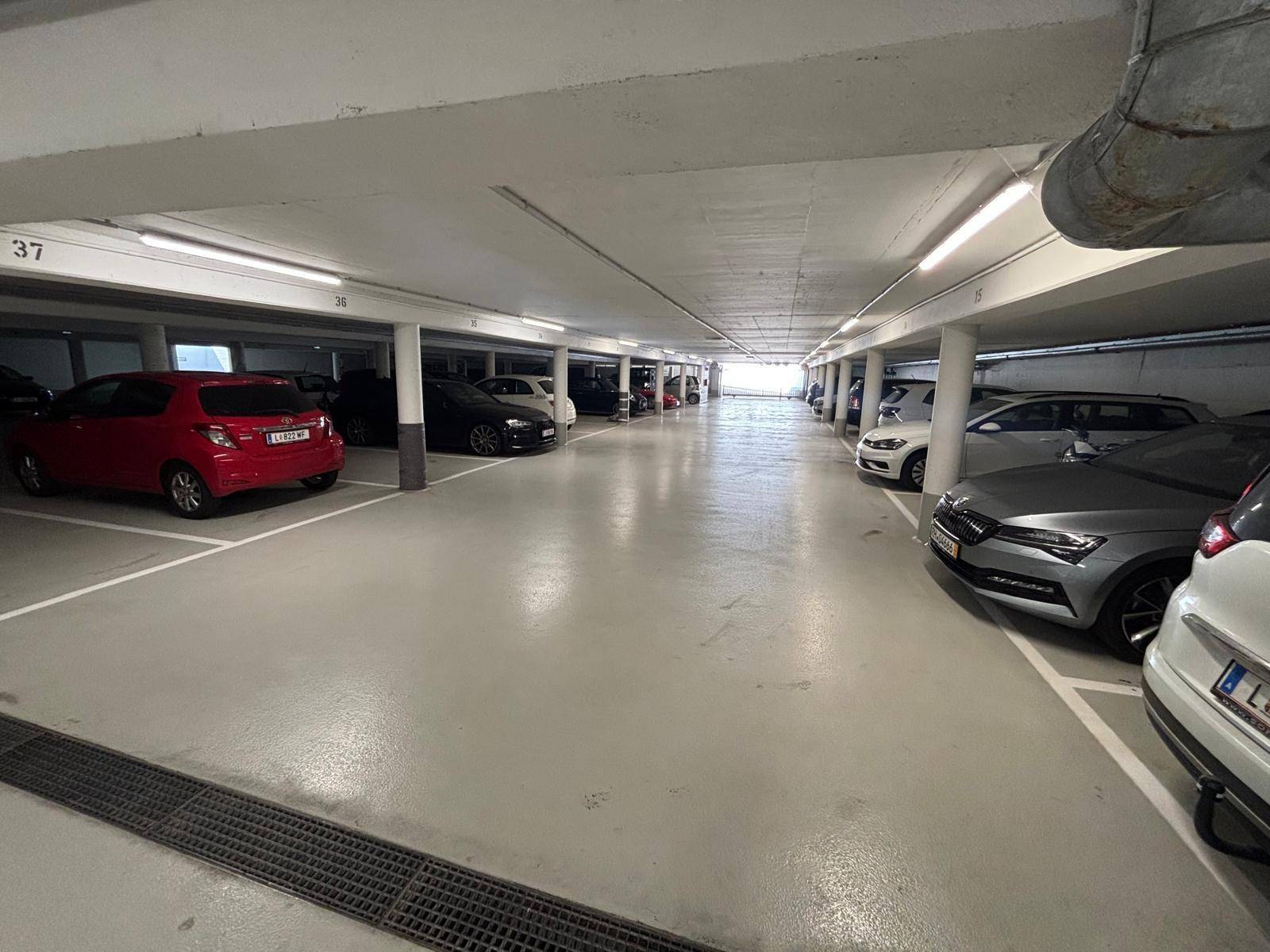 Langer Gang einer Tiefgarage mit vielen Parkplätzen und durchgehender Beleuchtung.