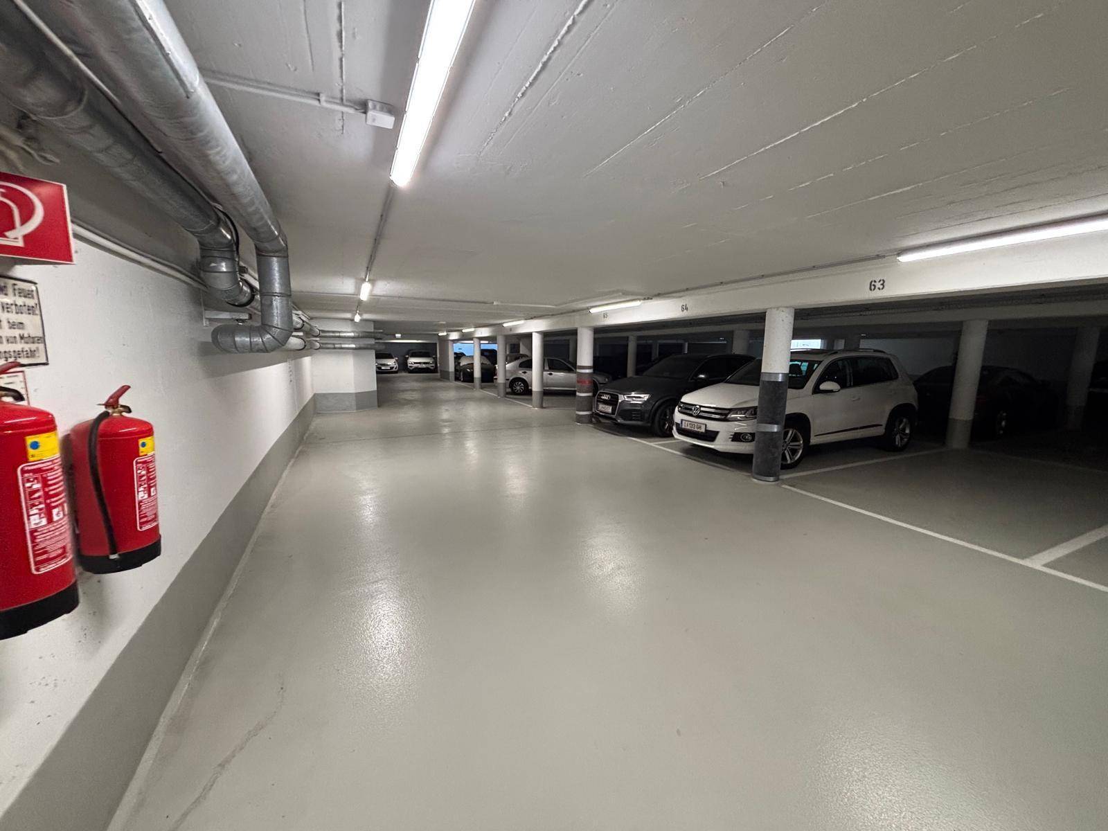 Saubere Tiefgarage mit Betonboden, sichtbaren Rohren an der Decke und Feuerlöschern.