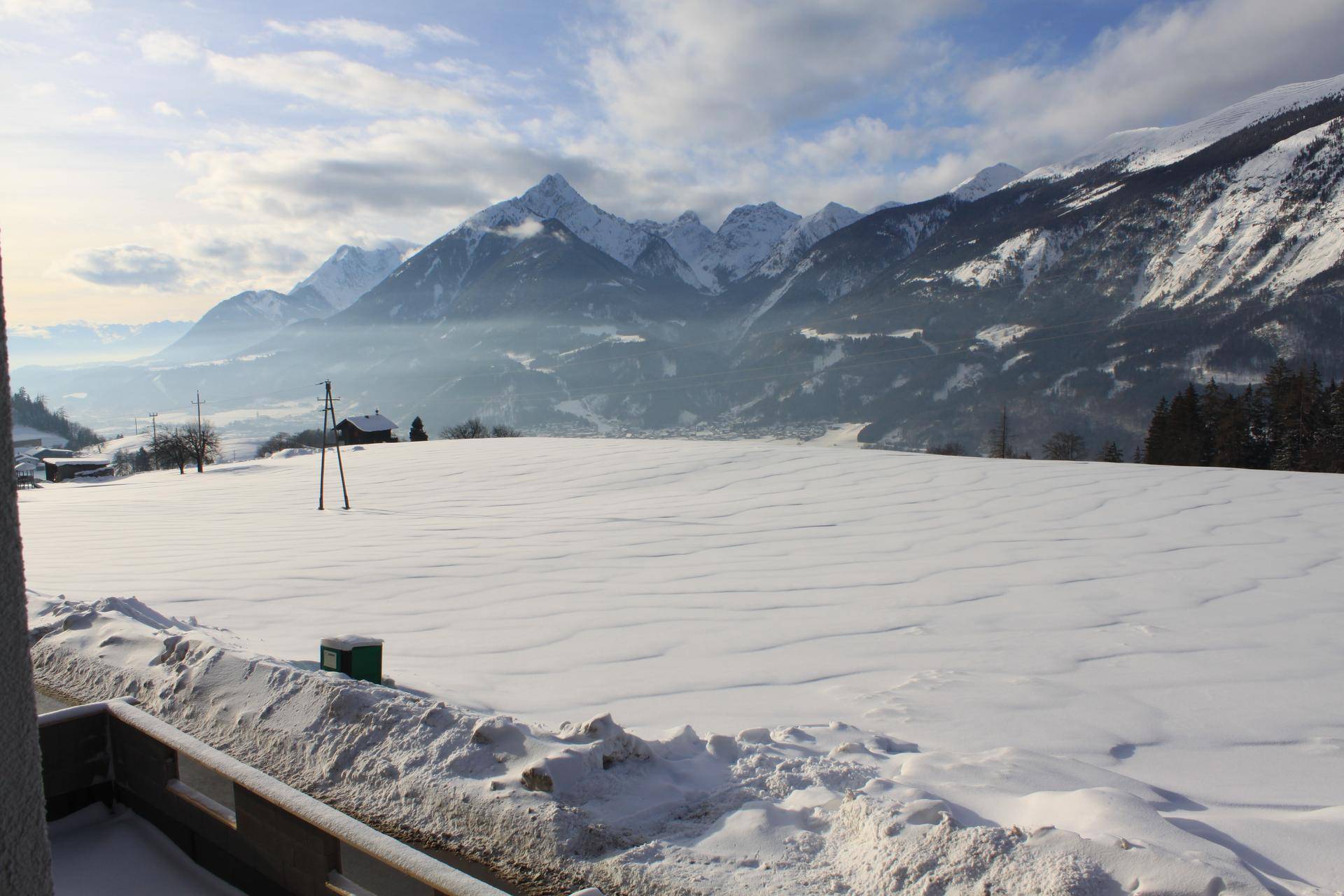 Weite, schneebedeckte Landschaft mit majestätischen Bergen im Hintergrund unter einem Winterhimmel.