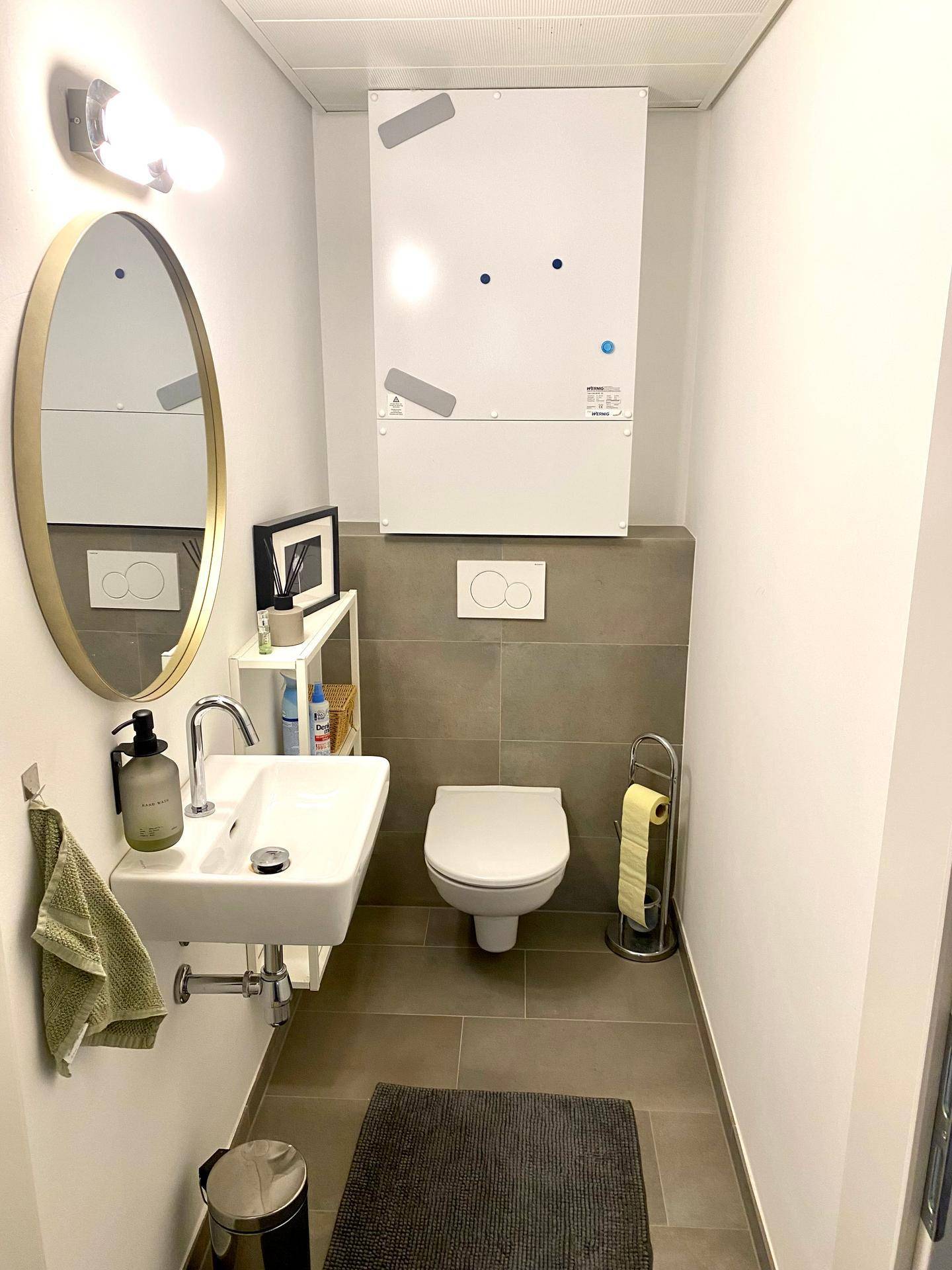 Kleines Gäste-WC mit Wand-WC, modernem Waschbecken und ovalem Spiegel.