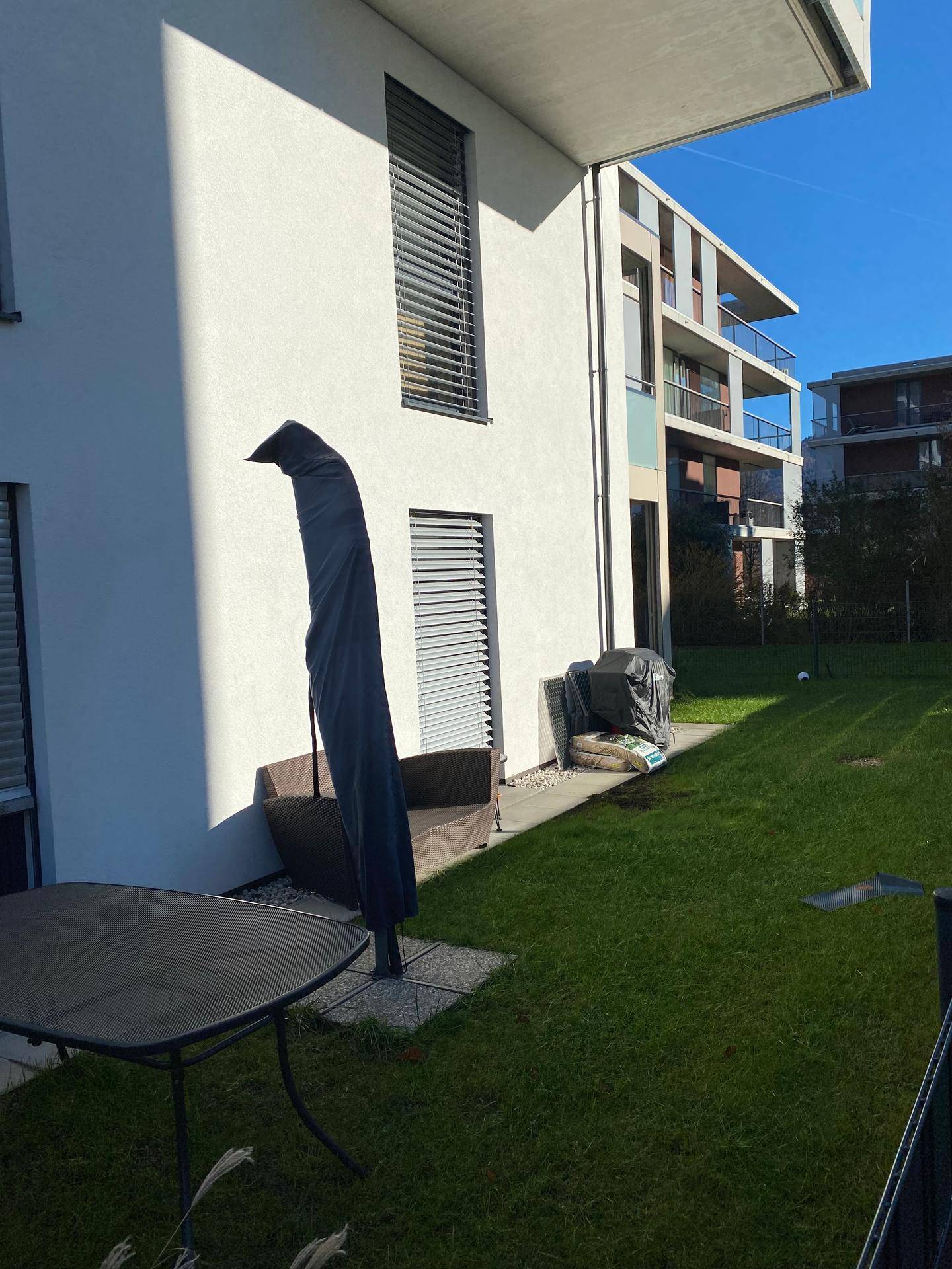 Sonniger Gartenbereich mit Rasenfläche und Sitzgelegenheit neben dem Gebäude.