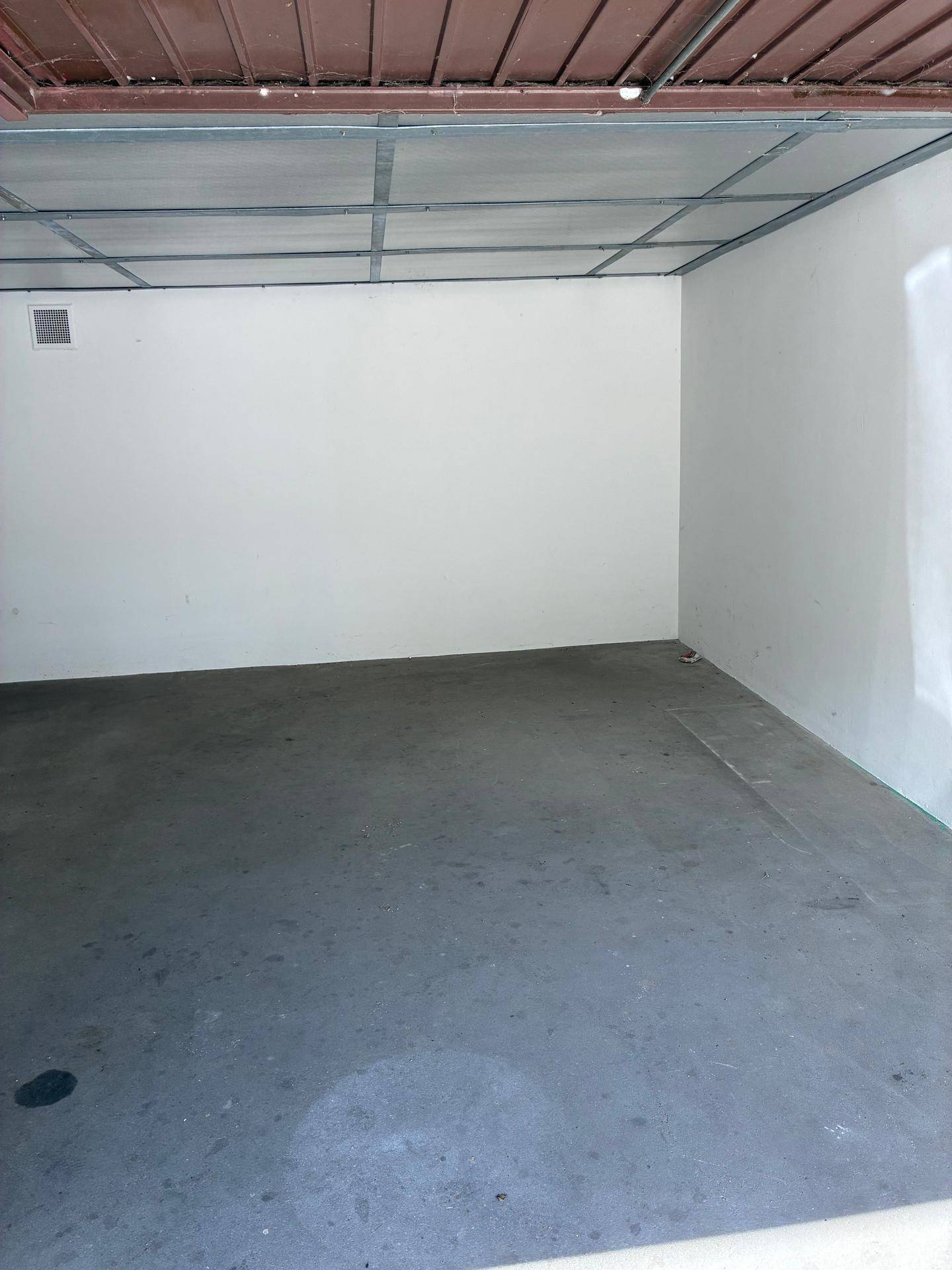 Leerer Garageninnenraum mit hellen Wänden, Betonboden und sichtbarer Deckenkonstruktion.