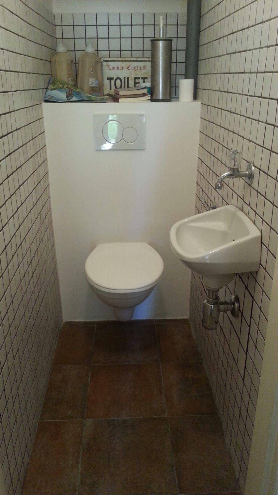 Kleines Gäste-WC mit wandhängender Toilette, kleinem Waschbecken und weiß gefliesten Wänden.