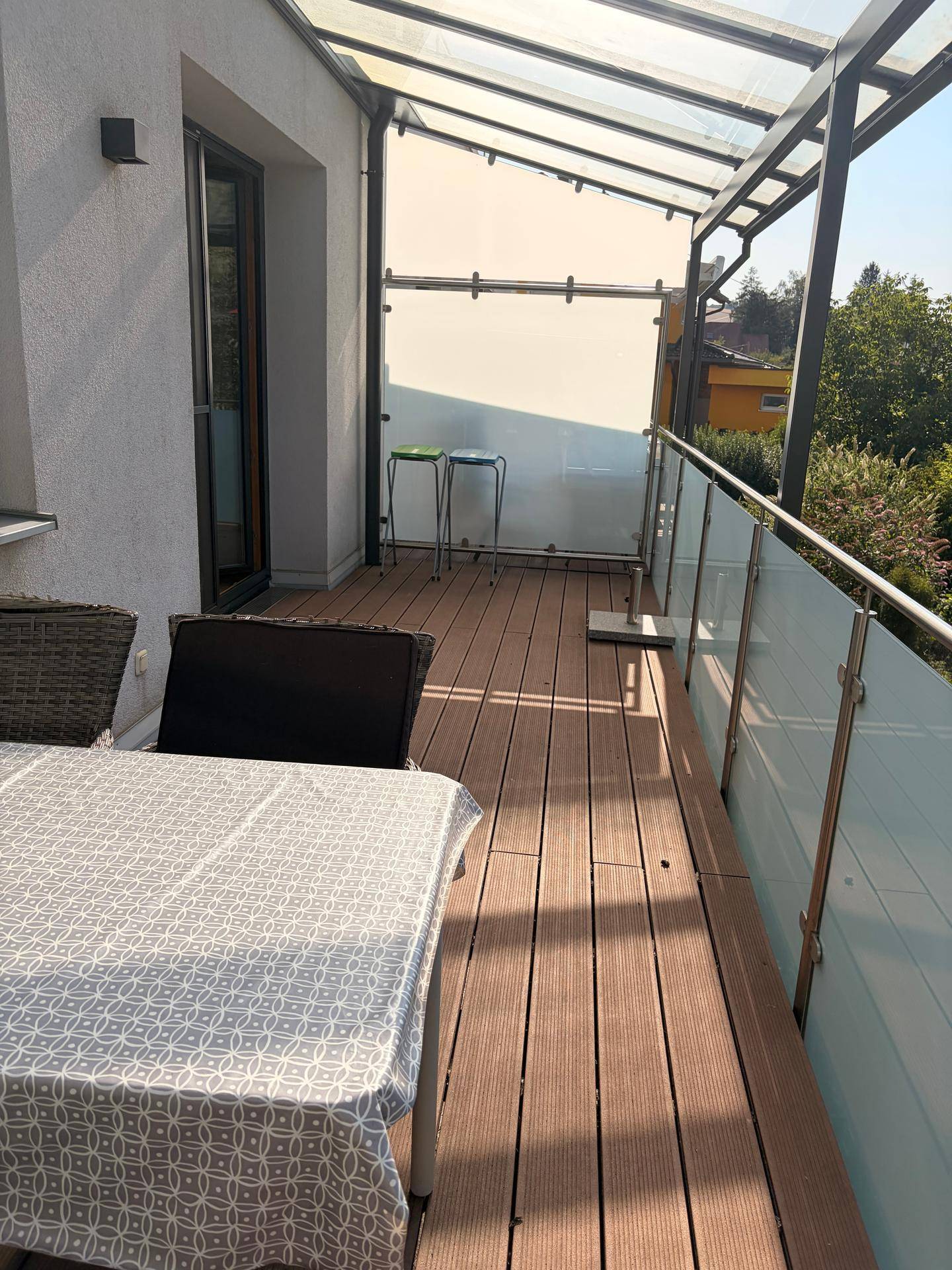 Sonnenverwöhnter Balkon mit Glasgeländer und Holzboden, bietet einen schönen Blick ins Grüne.