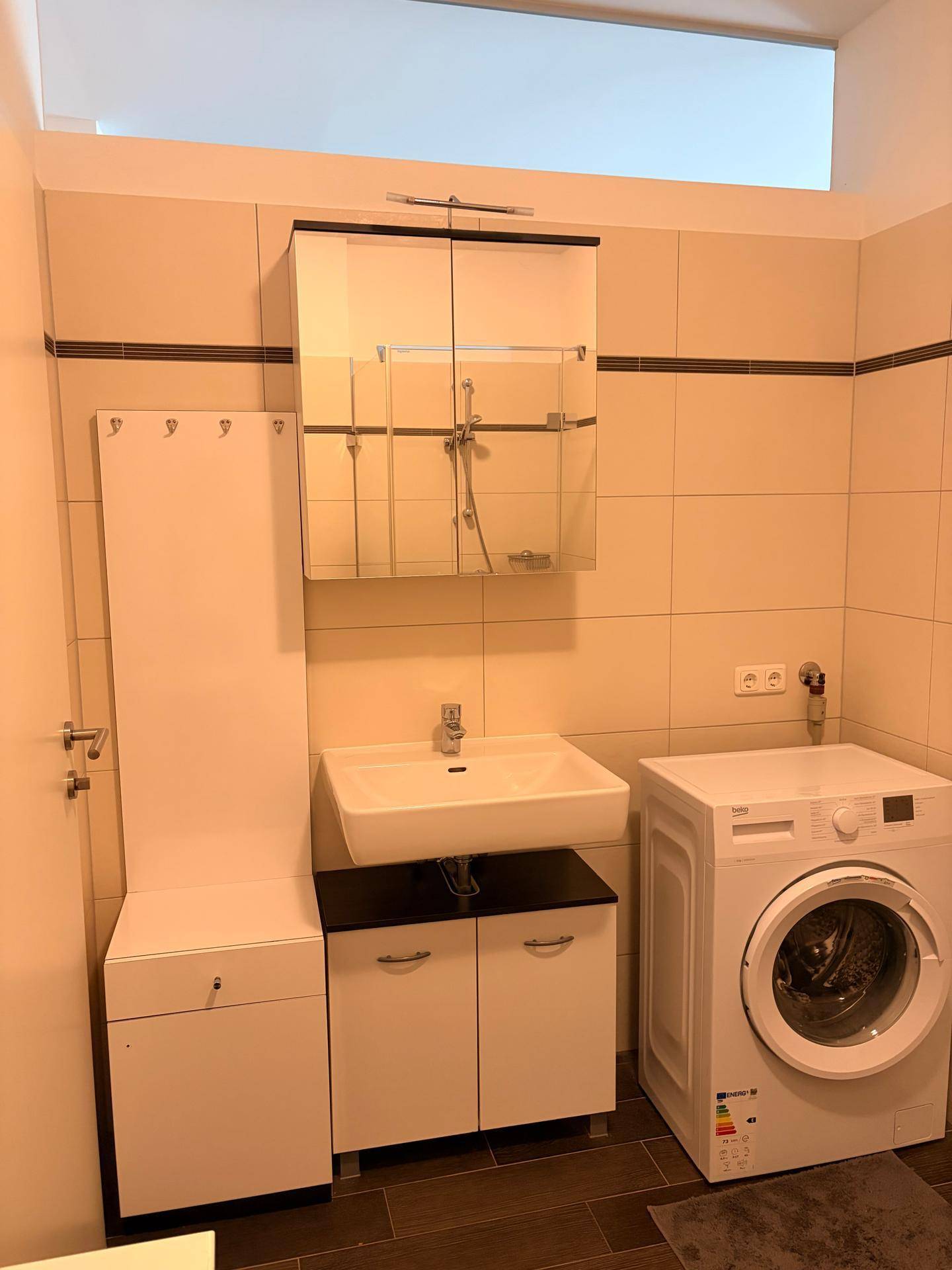 Praktisches Badezimmer mit Waschbecken, Spiegelschrank und integrierter Waschmaschine.