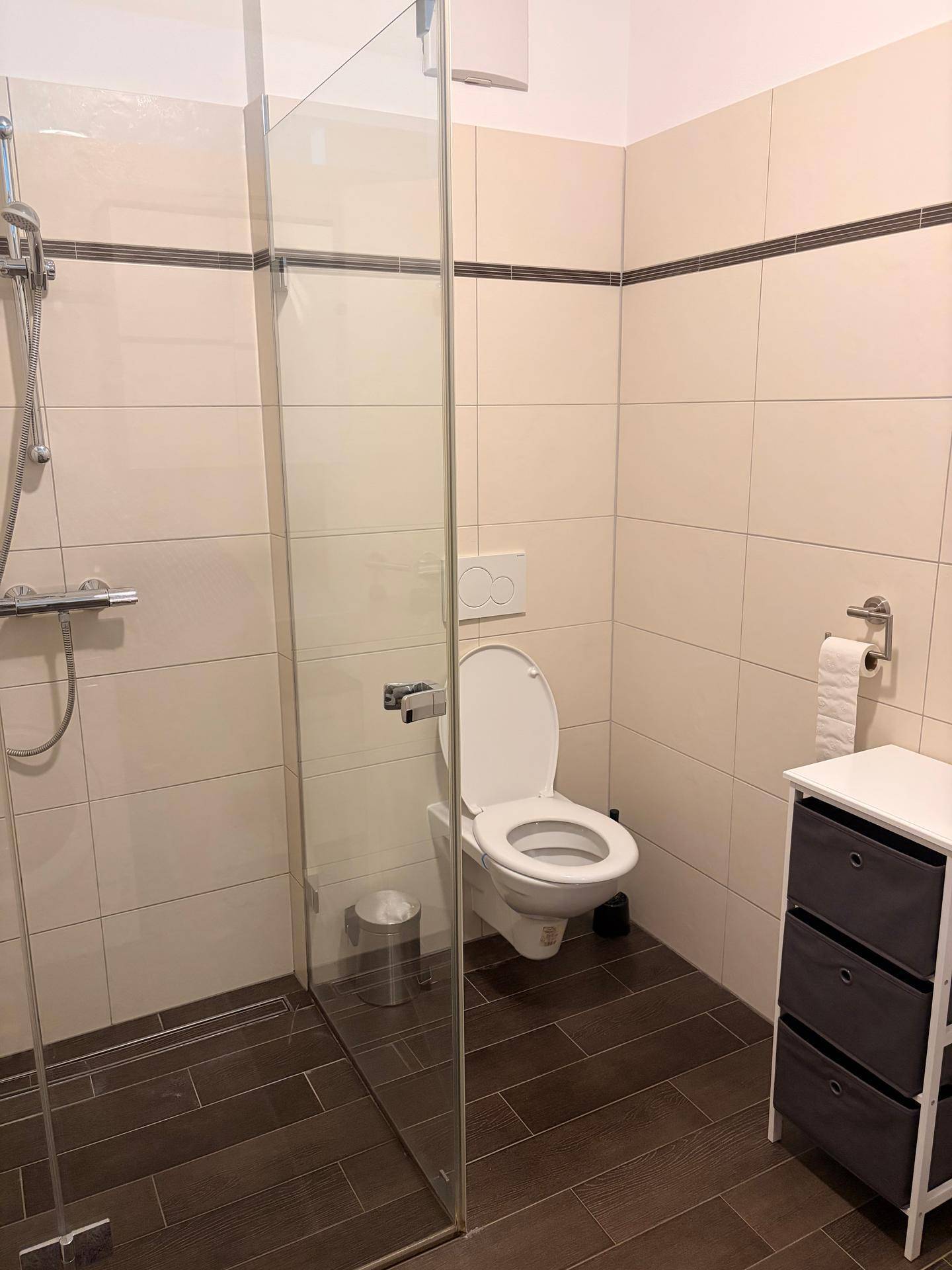 Modernes Badezimmer mit ebenerdiger Dusche, wandhängendem WC und dunklen Bodenfliesen.