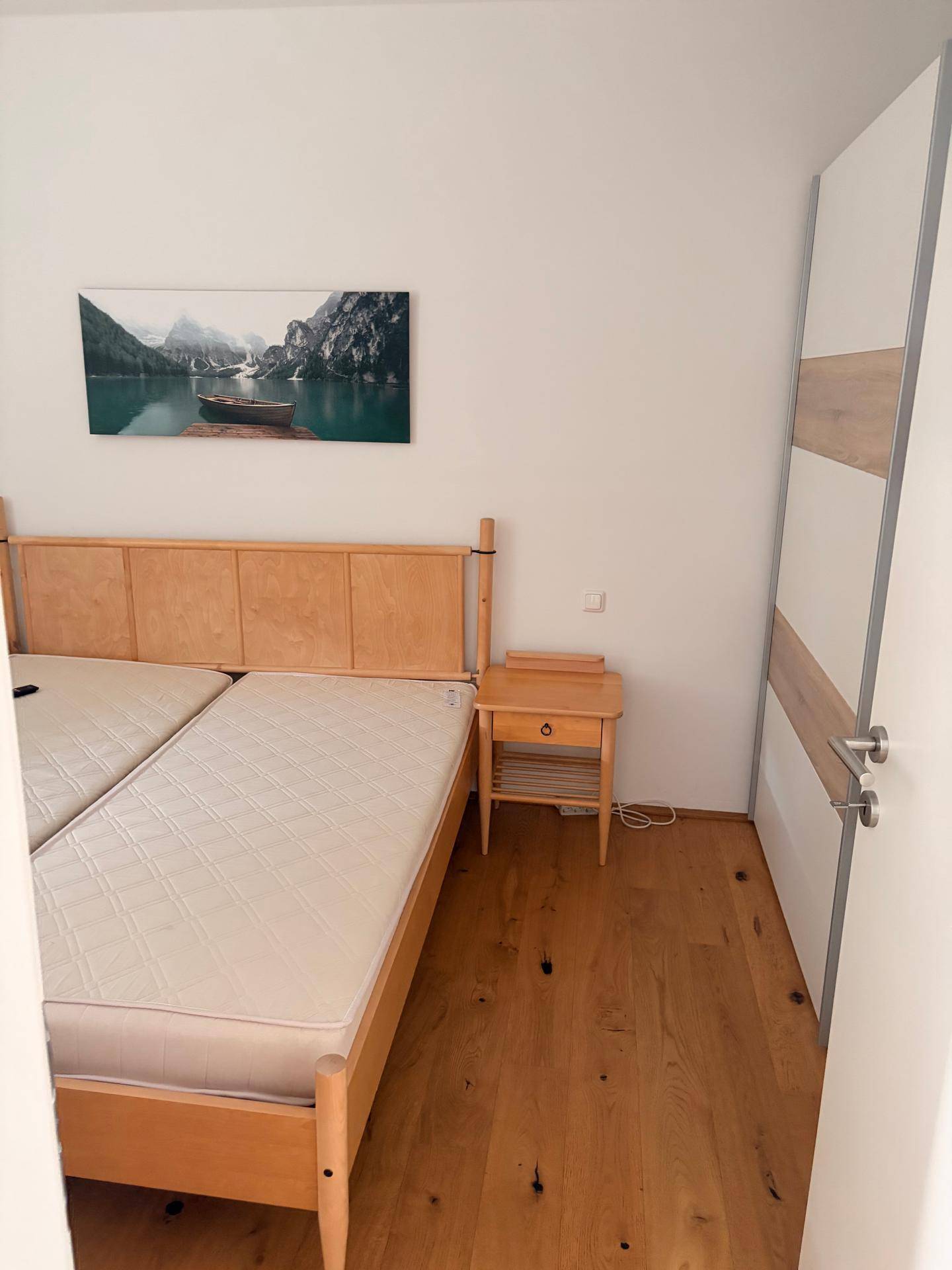 Gemütliches Schlafzimmer mit Holzbett, Nachttisch und Parkettboden, hell und einladend.