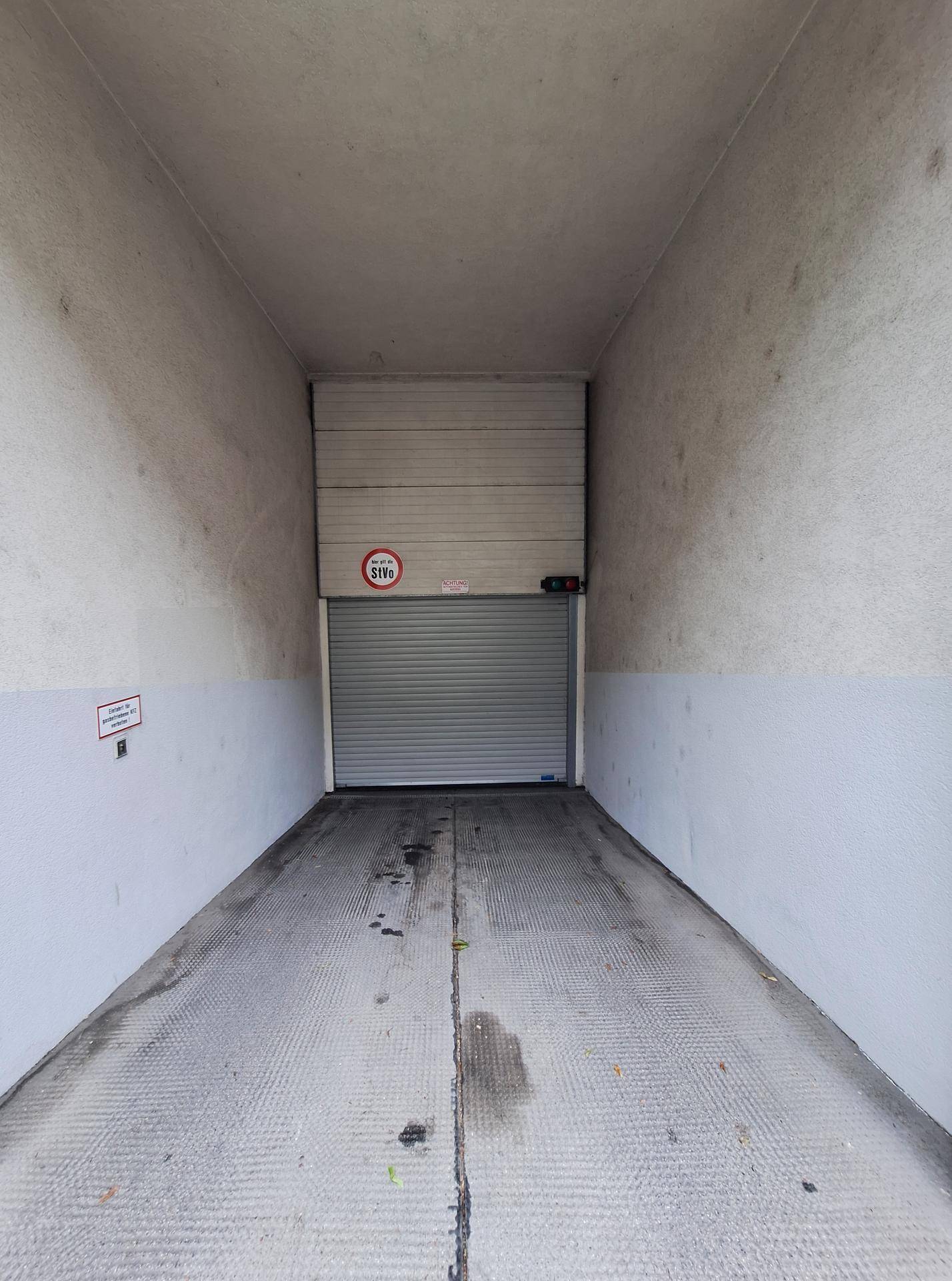 Einfahrtstunnel einer Tiefgarage mit geschlossenem Rolltor und Betonwänden.