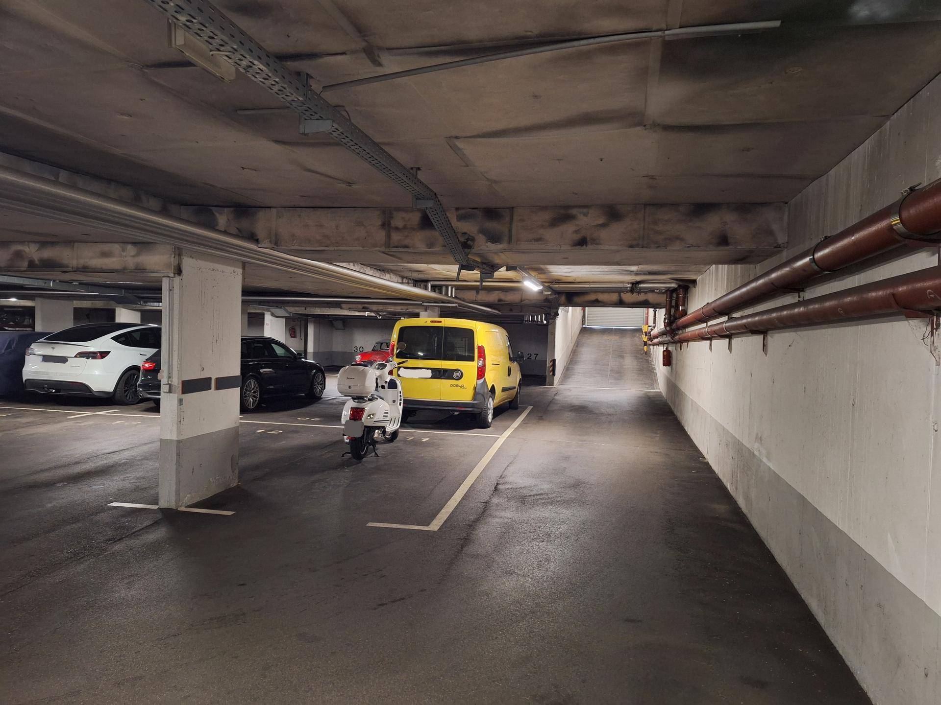 Tiefgarage mit geparkten Autos und einer Rampe, die zur Ausfahrt führt.