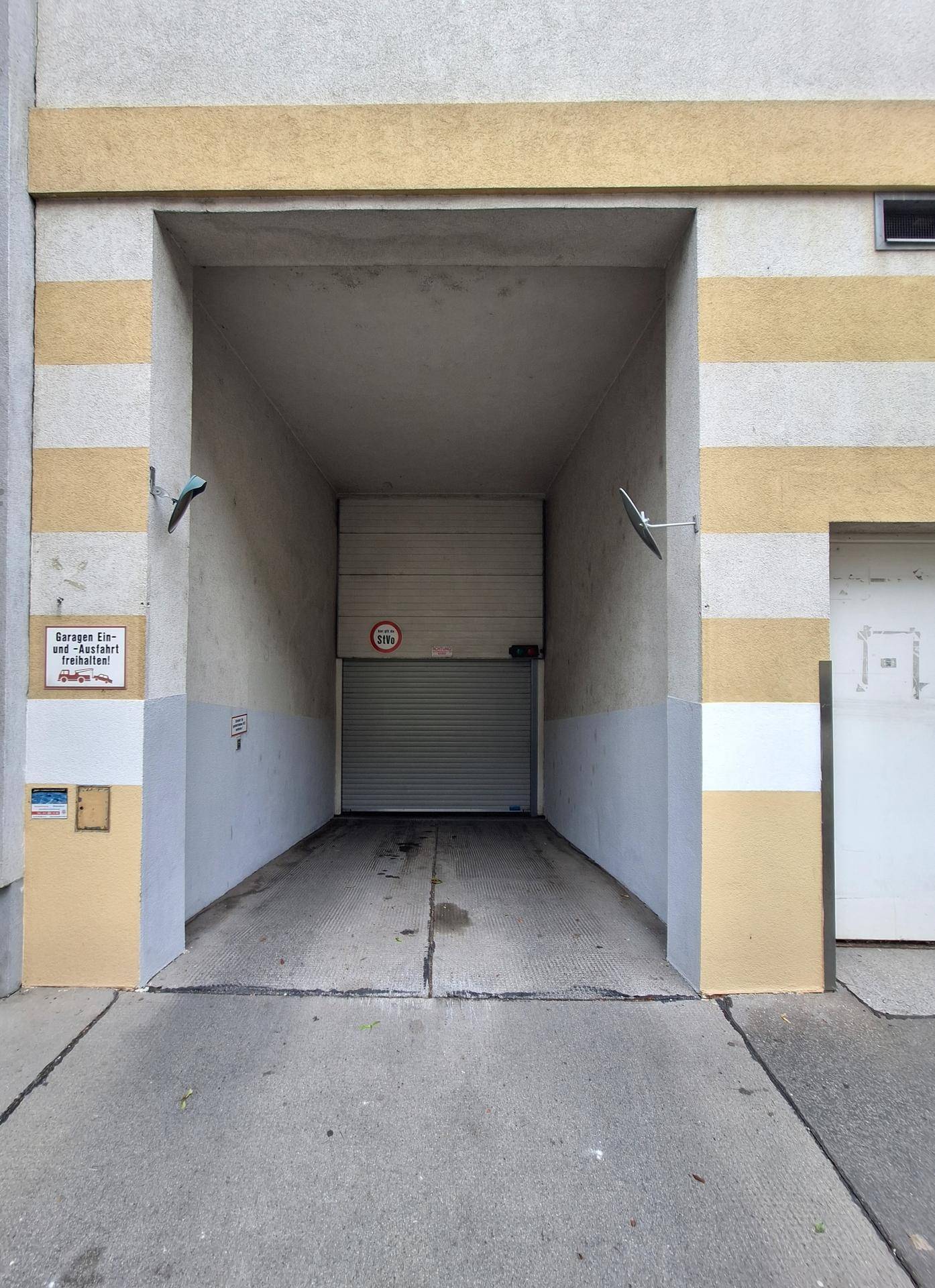 Garageneinfahrt mit geschlossenem Rolltor und gelb-grauer Fassade.