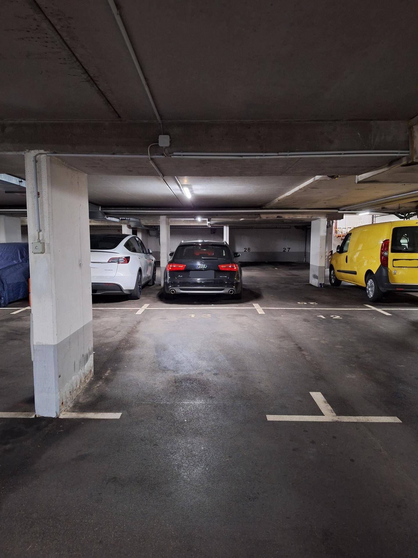 Tiefgarage mit geparkten Autos, Betonstützen und Beleuchtung.