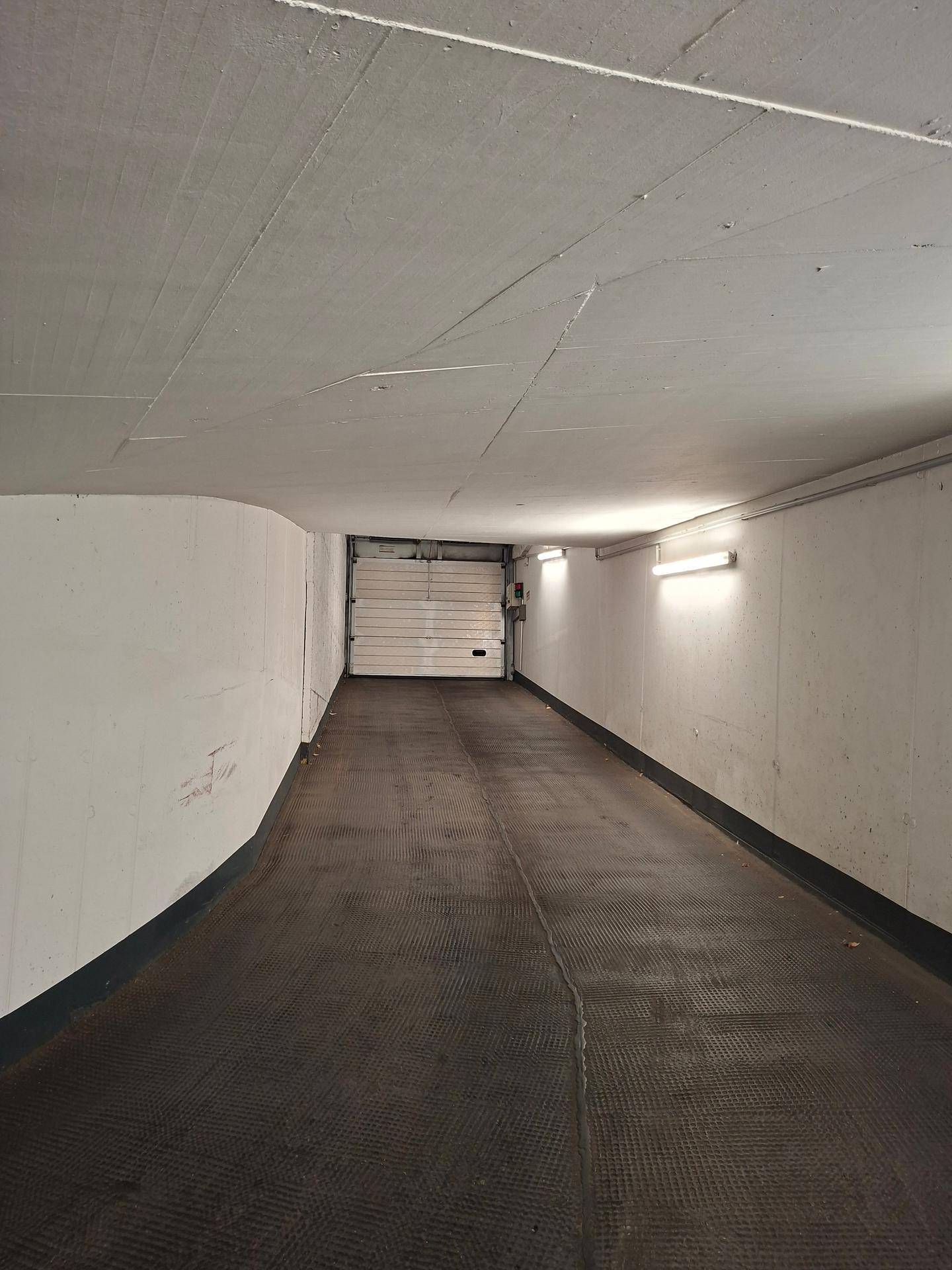 Gerade Einfahrtsrampe einer Tiefgarage mit geschlossenem Garagentor am Ende.