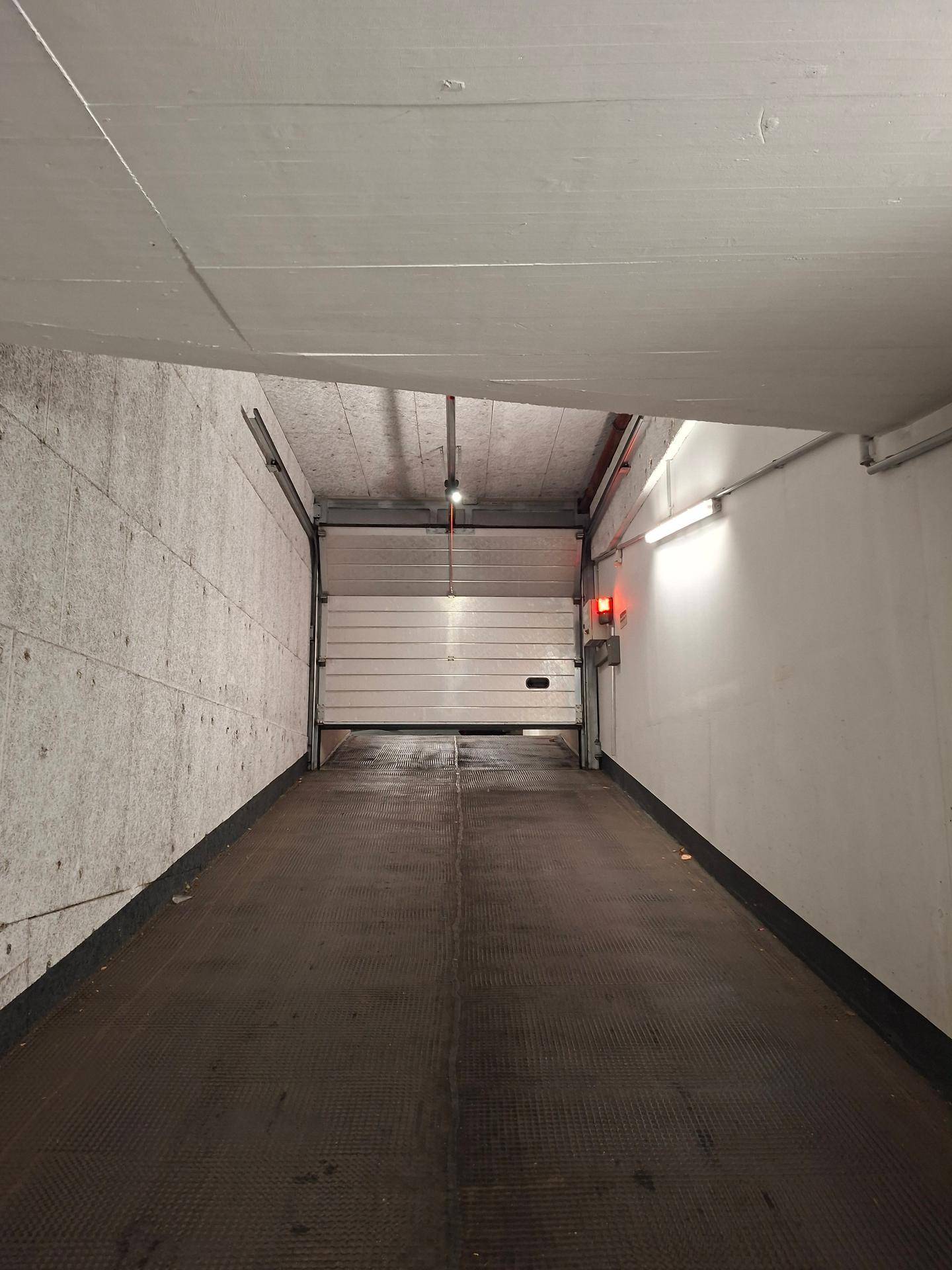 Einfahrtsrampe einer Tiefgarage mit offenem Garagentor und roter Warnleuchte.