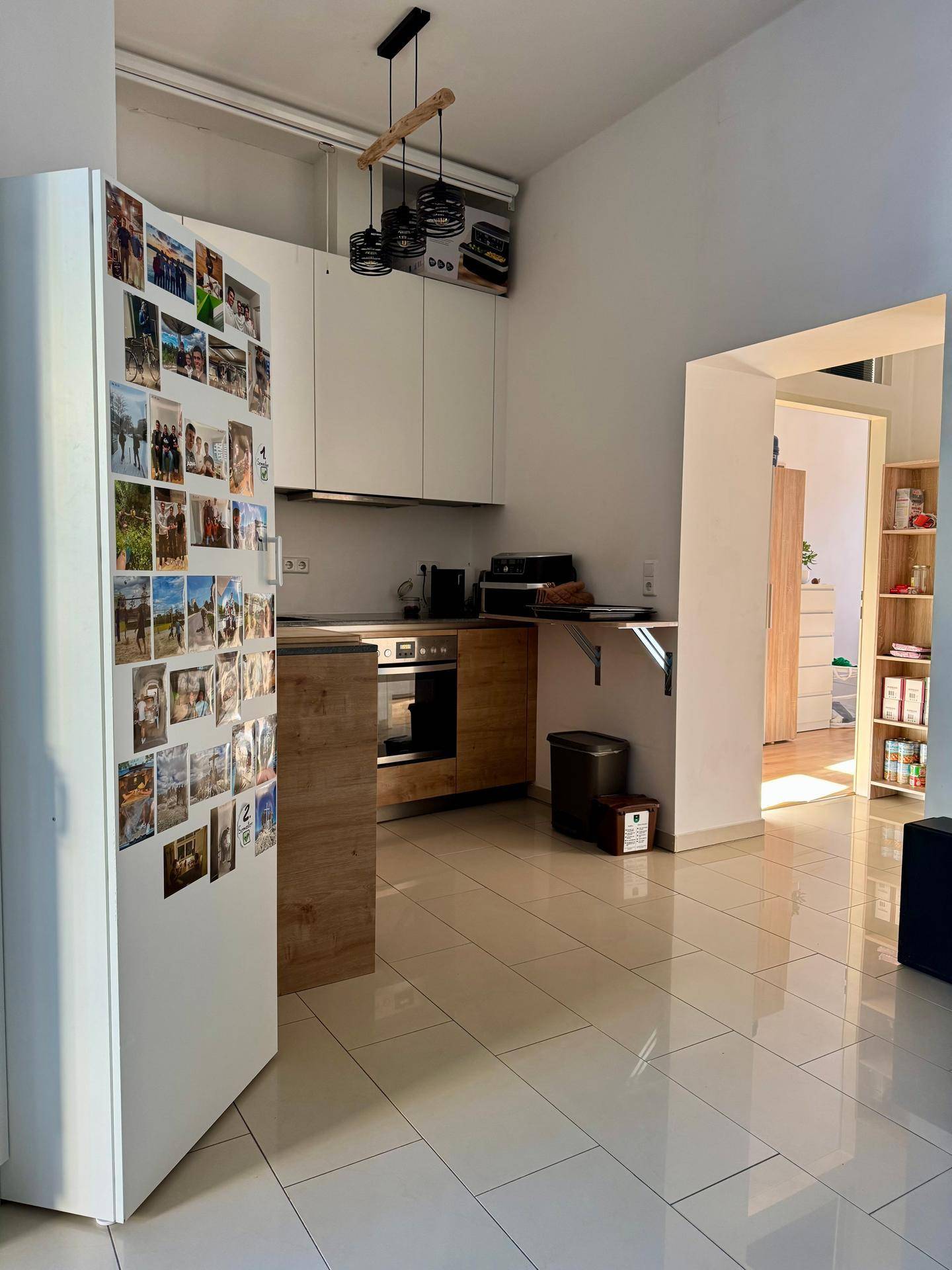 Funktionale Küche mit weißen Oberschränken, Holzakzenten und einem Kühlschrank, der mit Fotos dekoriert ist.