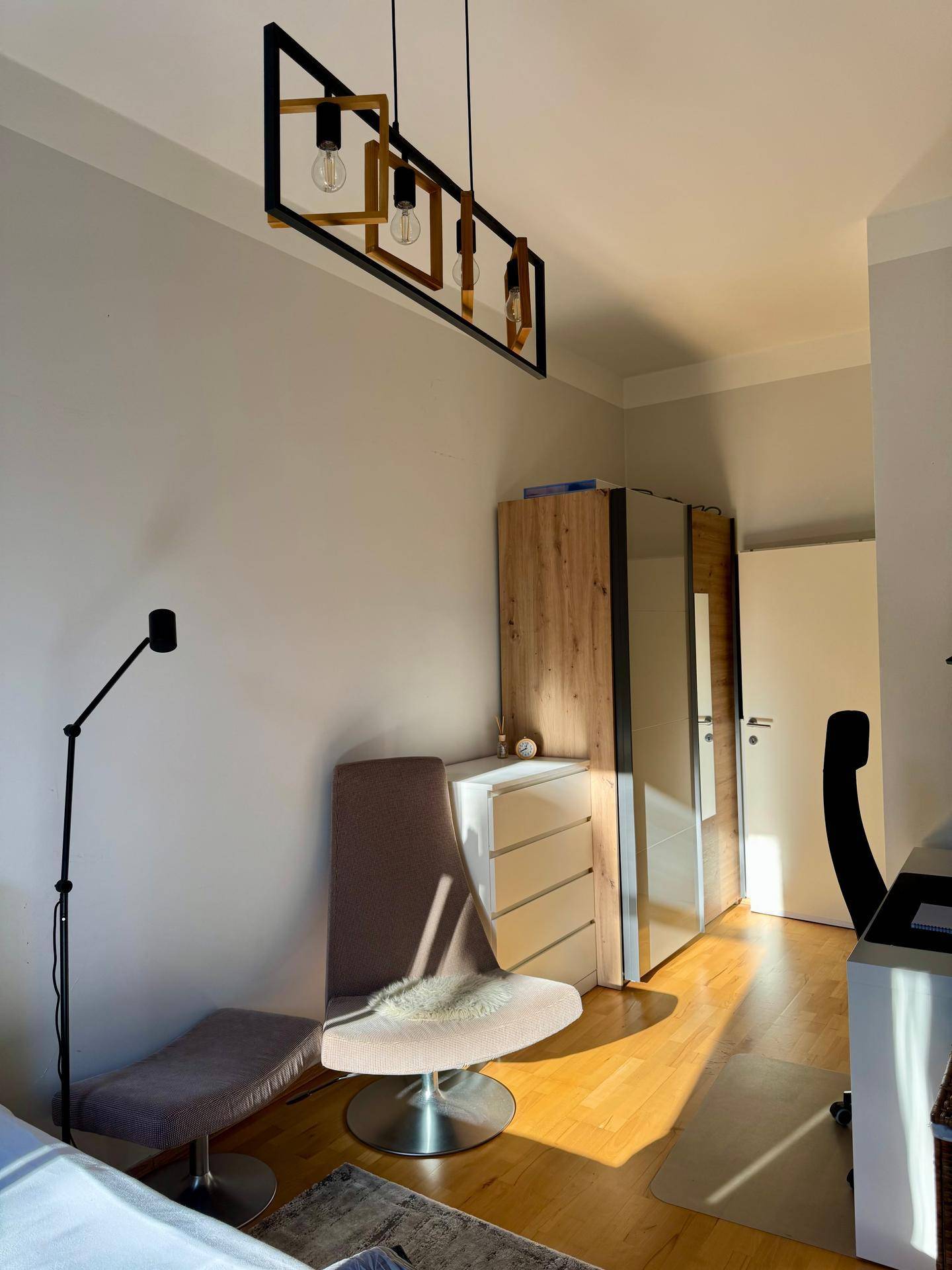Schlafzimmerbereich mit Kleiderschrank, Kommode und moderner Deckenleuchte, durchflutet von Sonnenlicht.