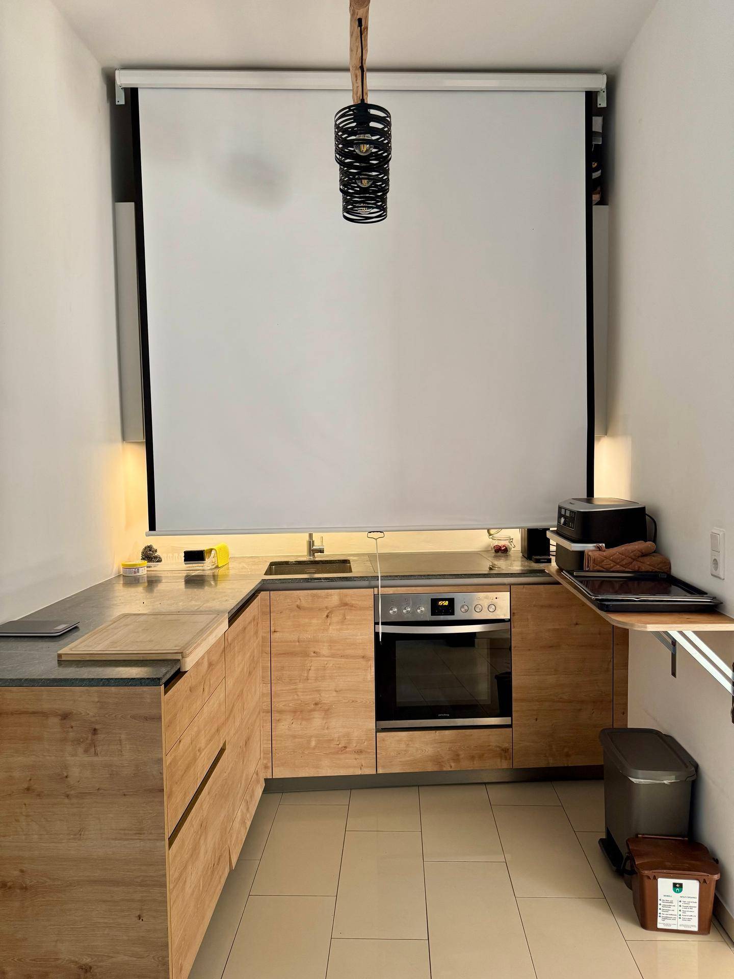 Küchenzeile mit Holzfronten, integriertem Backofen und Induktionskochfeld unter einer Projektionsfläche.