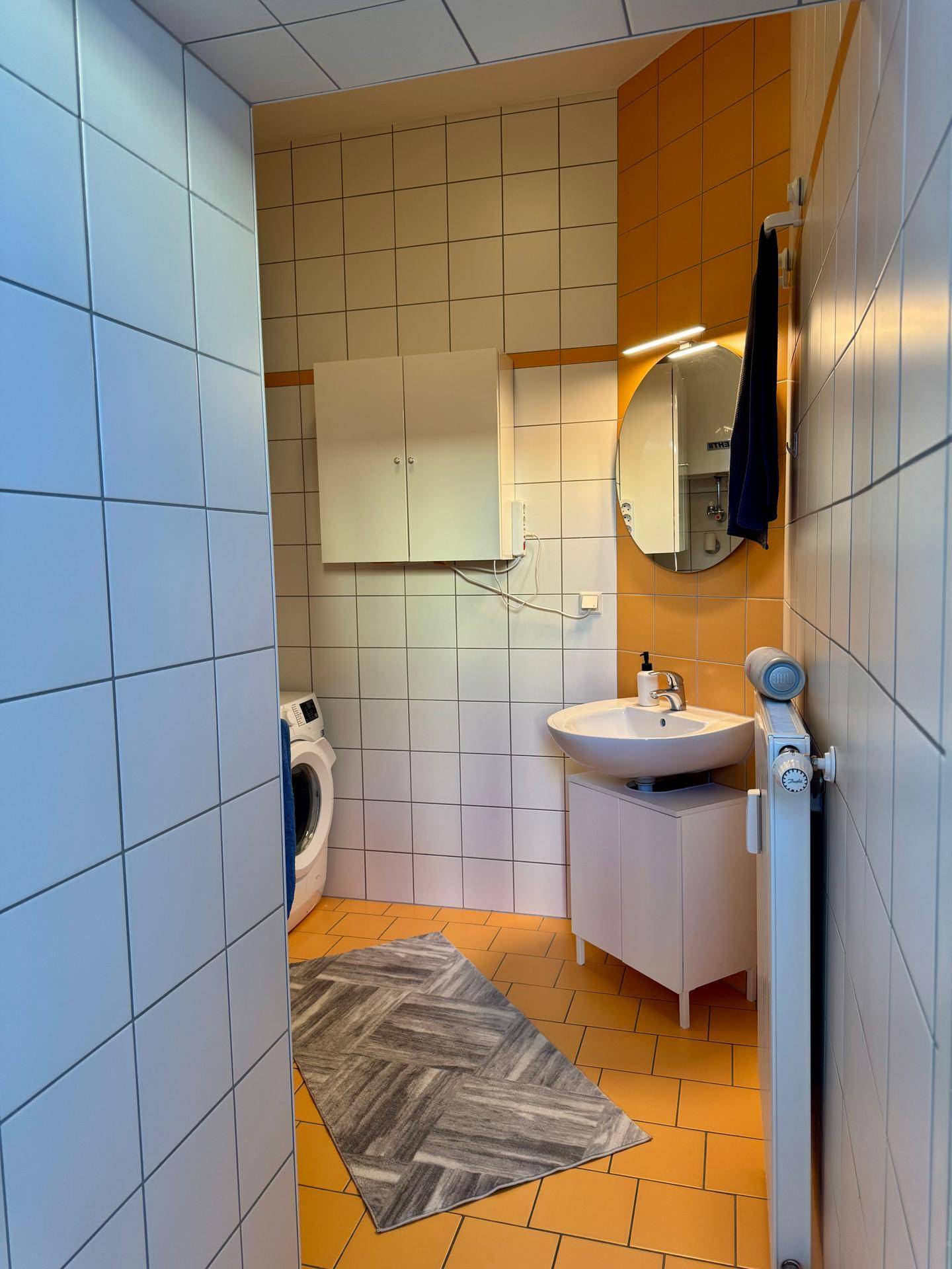 Badezimmer mit auffälligen orange-weißen Fliesen, Waschbecken und einer Waschmaschine.
