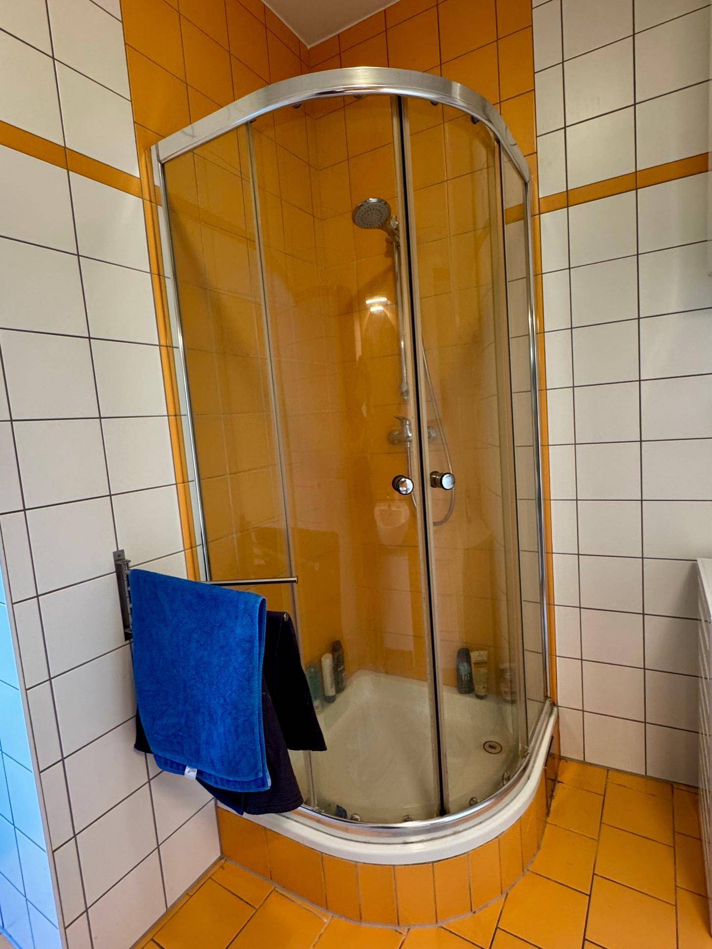 Duschkabine in einem farbenfrohen Badezimmer mit orangefarbenen und weißen Fliesen.