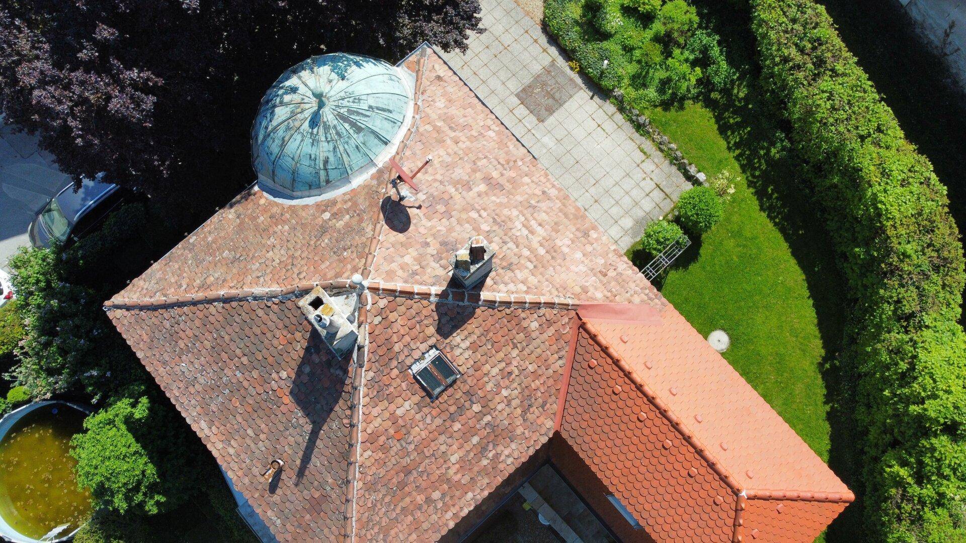 Luftaufnahme des Daches eines historischen Gebäudes mit Kuppel, Ziegeln und viel Grün.