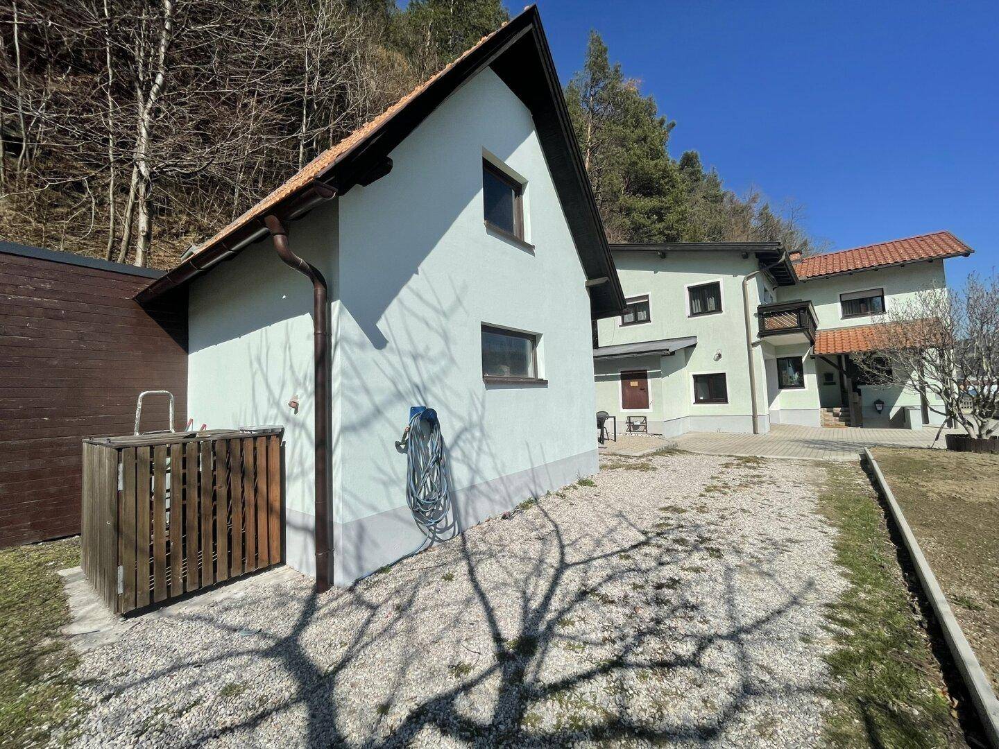 Außenansicht eines Nebengebäudes mit Satteldach und angrenzendem Hauptgebäude im Grünen.