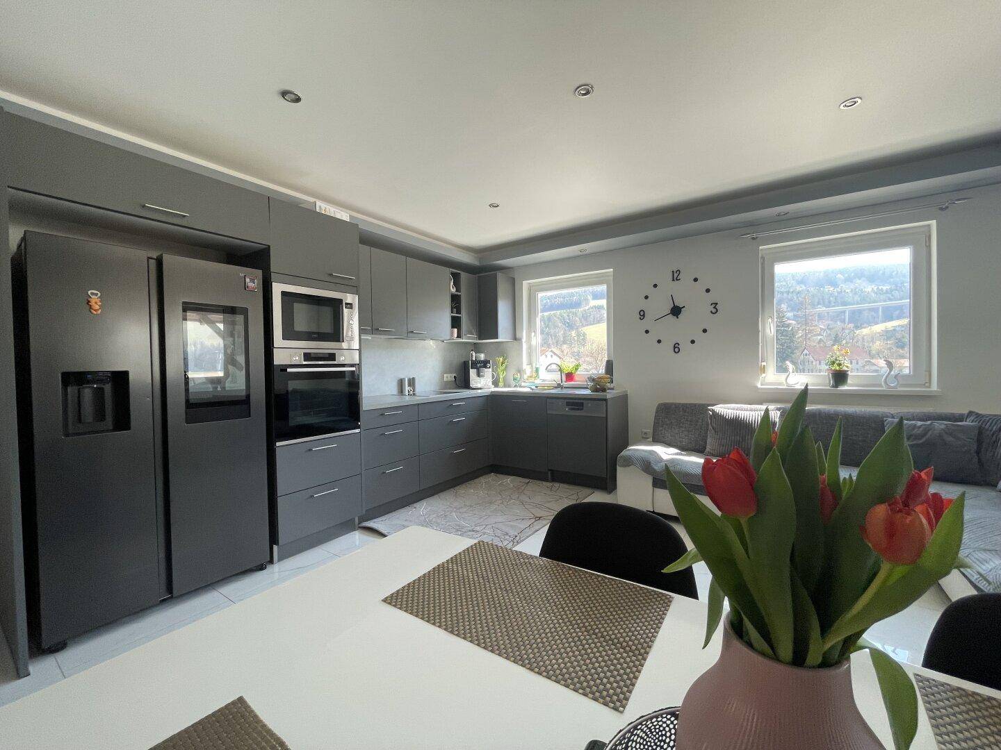 Moderne Küche mit grauen Fronten und integrierten Geräten, offen zum Wohnbereich mit Sofa.