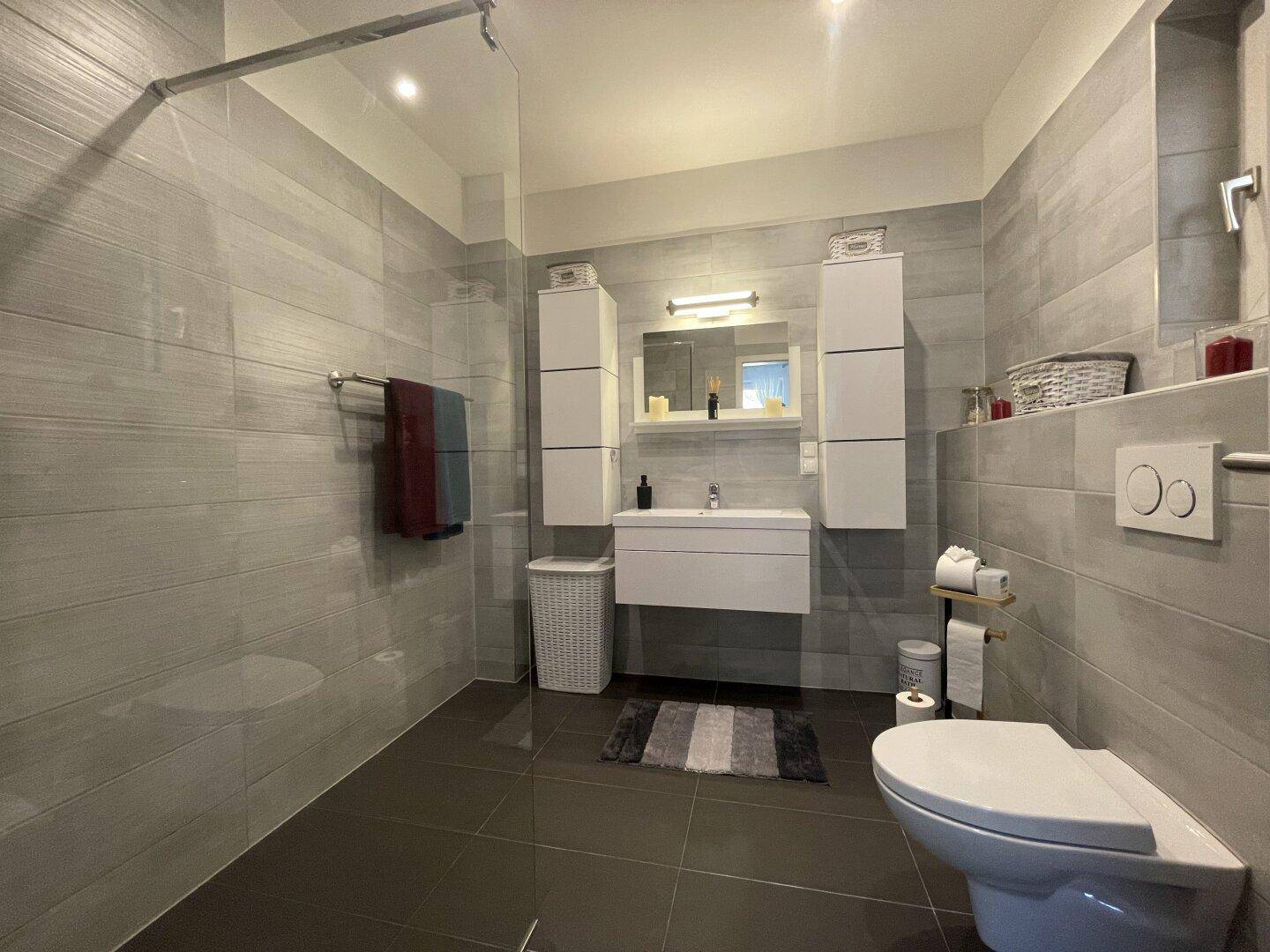 Modernes Badezimmer mit grauen Fliesen, ebenerdiger Dusche und wandhängendem WC.