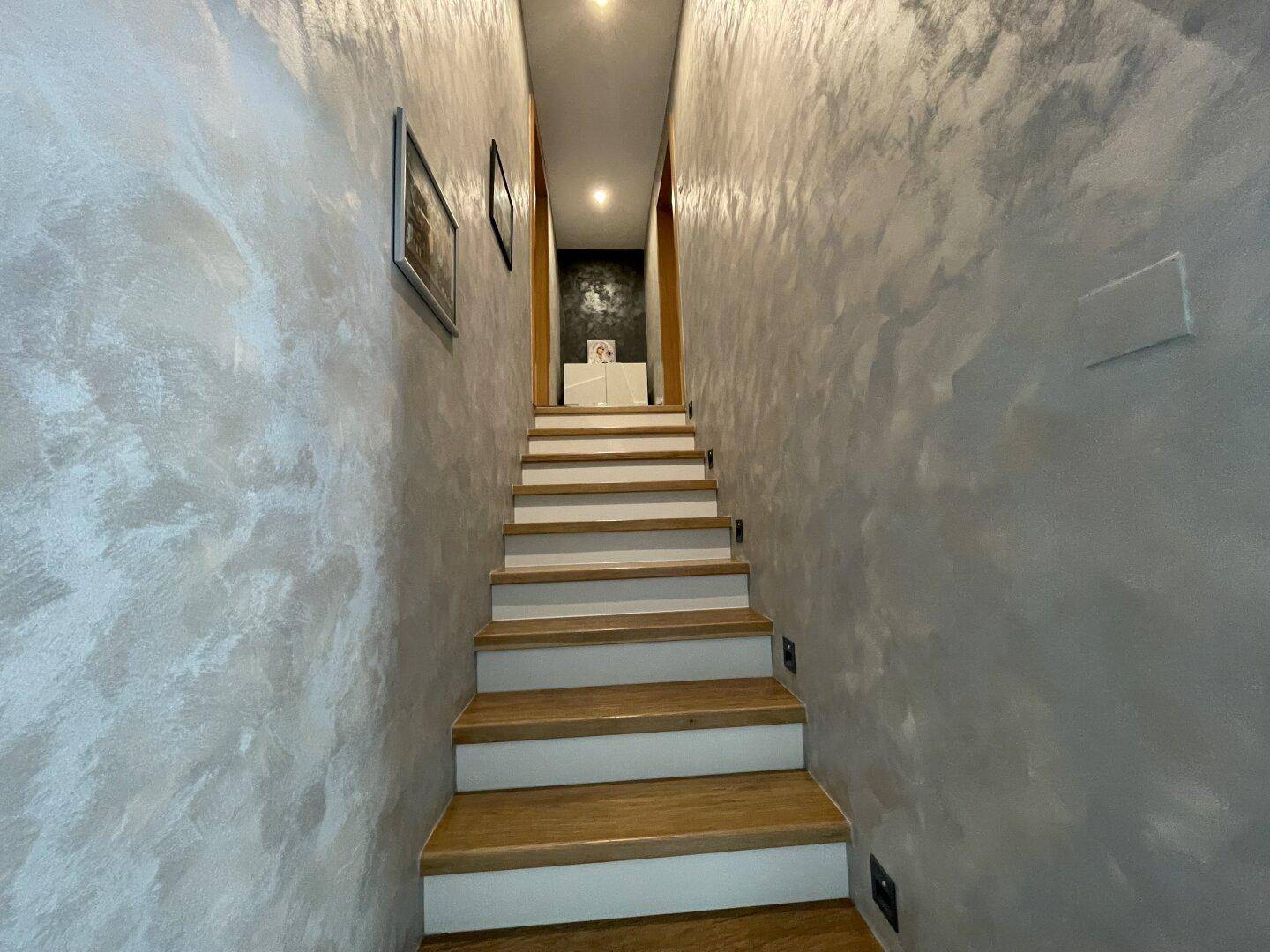 Treppenaufgang mit modern gestalteten Wänden und Holzstufen, die nach oben führen.