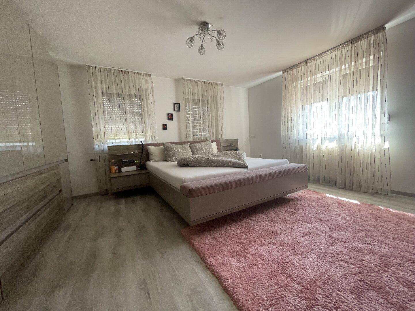 Geräumiges Schlafzimmer mit Doppelbett, Laminatboden und großem Fenster mit Vorhängen.